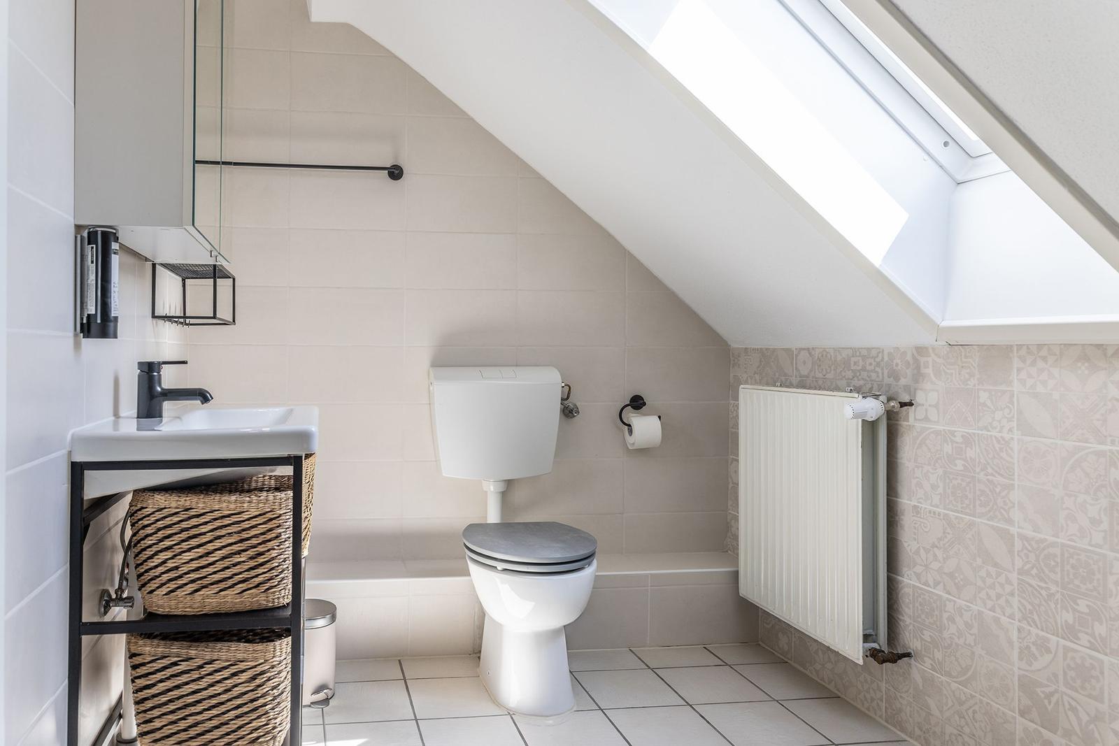 Badezimmer mit Toilette, Waschbecken und Dachfenster. Wandfliesen und Heizkörper sichtbar.