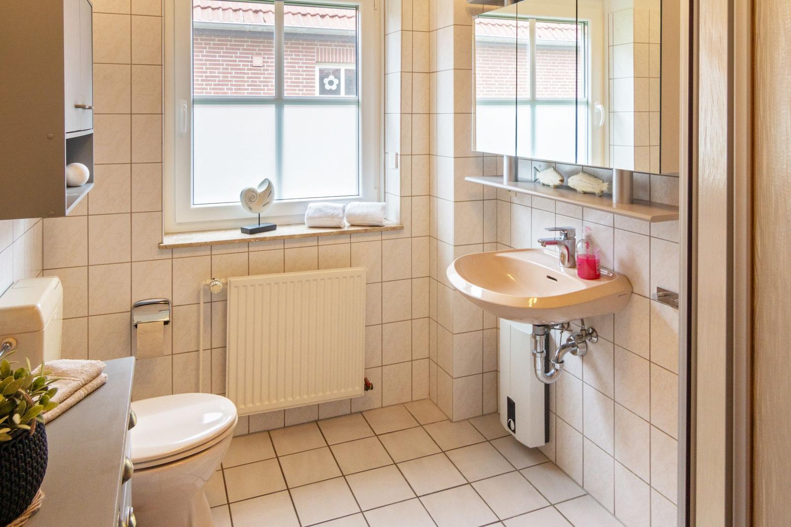 Badezimmer mit Waschbecken, Toilette und Fenster mit Blick auf Hausfassade.
