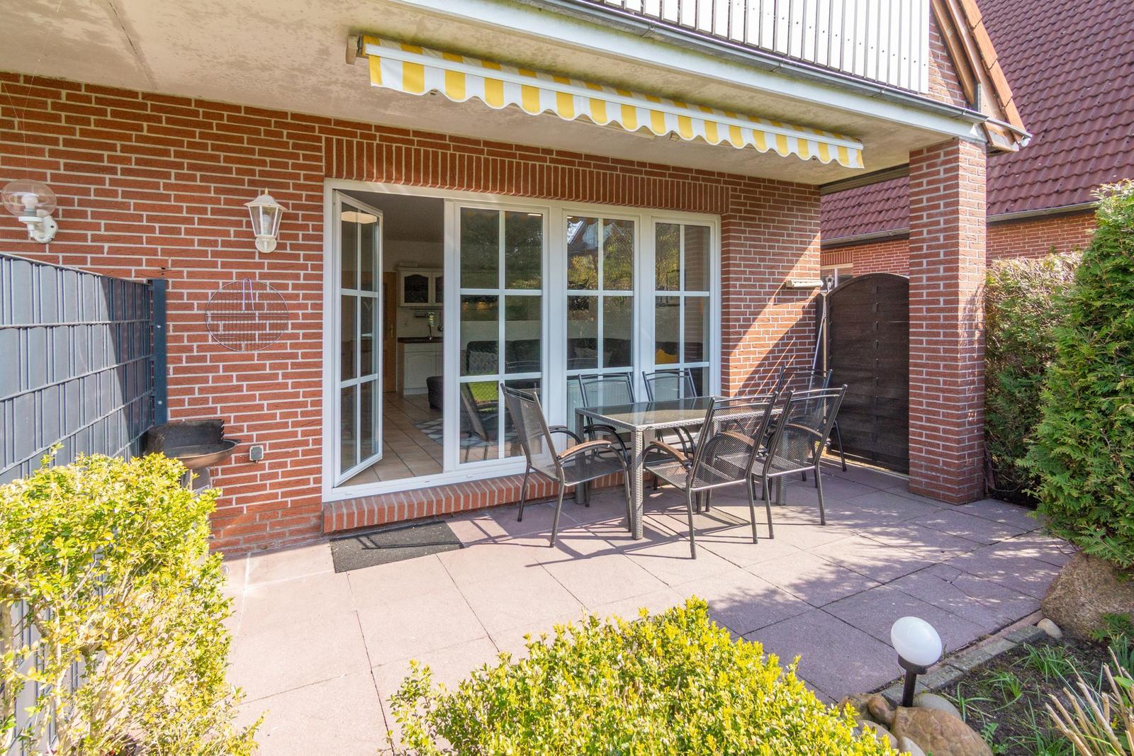 Terrasse mit Sitzgruppe, Grill und Glas-Tür zum Haus. Gelb-weiße Markise.