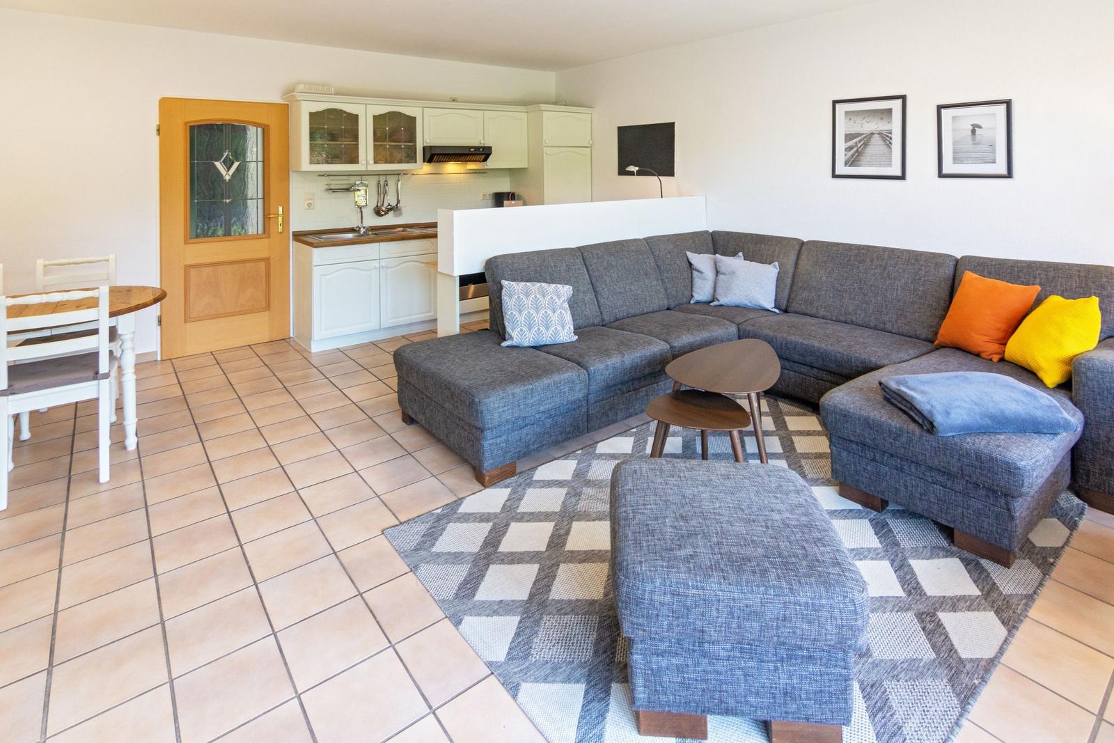 Wohnzimmer mit grauem Sofa, Teppich und Küchenbereich im Hintergrund.