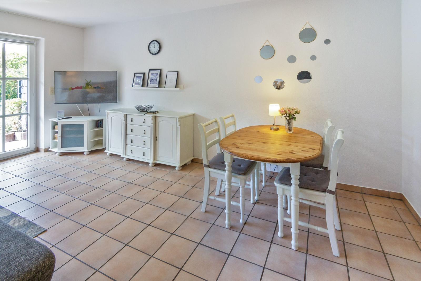 Essbereich mit runden Tisch und weißen Stühlen. Wand mit Spiegeln und Fernseher.