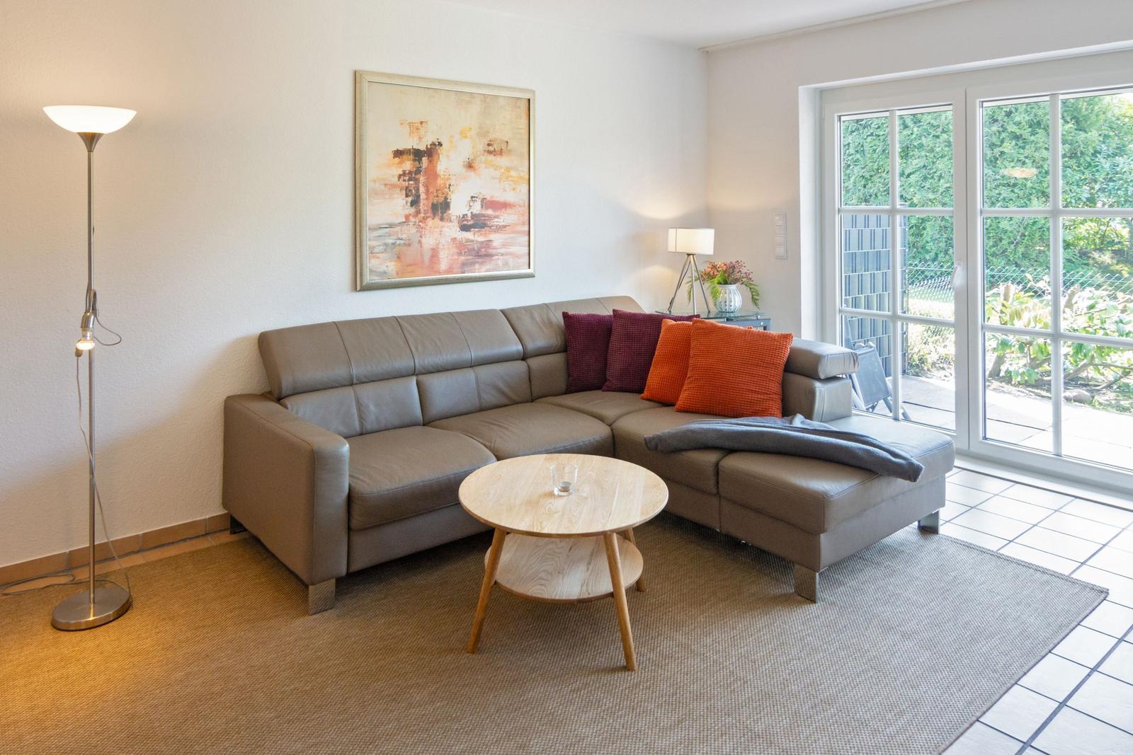 Ein Wohnzimmer mit einem grauen Sofa, einem runden Tisch und einer Glastür zum Garten.