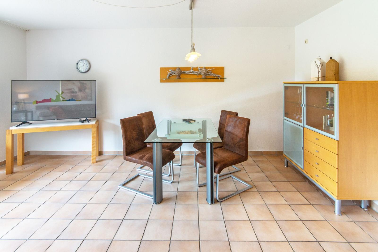 Esszimmer mit Glas-Tisch, vier braunen Stühlen, Fernseher und Sideboard.
