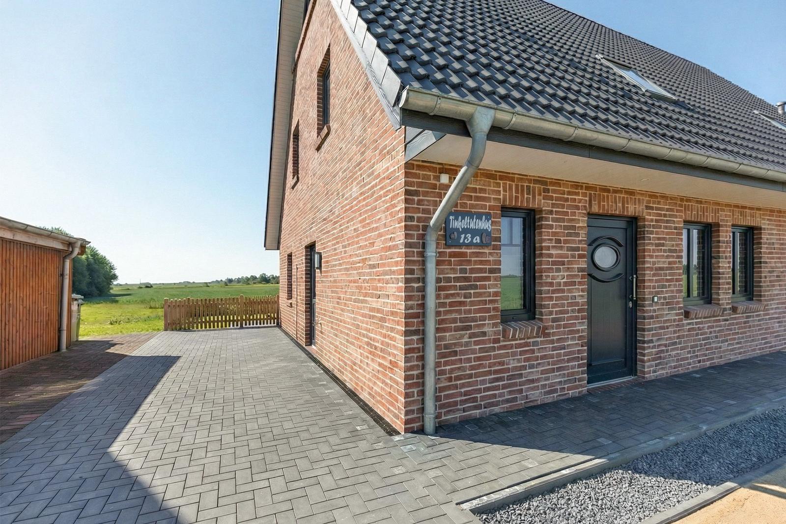 Modernes Backsteinhaus mit dunkler Tür und Dach, gepflasterter Hof und Holzzaun im Hintergrund.