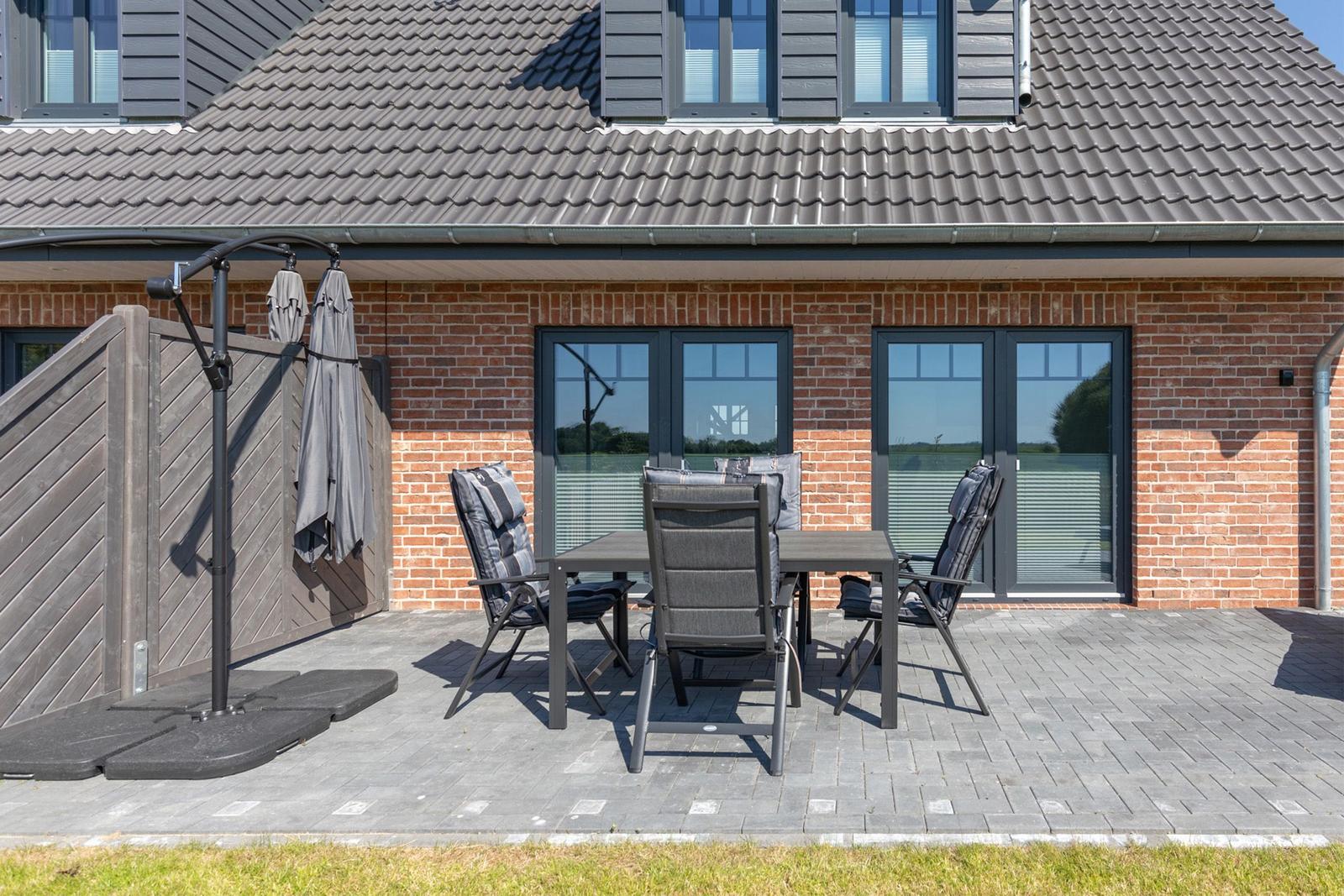 Terrasse mit Tisch, Stühlen und Sonnenschirm vor einem Backsteinhaus.