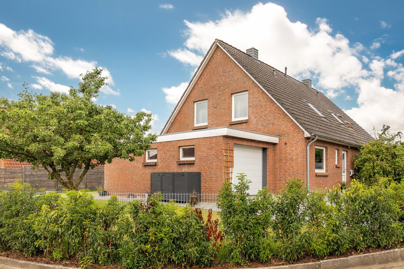 Ein zweistöckiges Haus mit rotem Backstein, Dach mit Schiebedach und Garten mit Sträuchern.