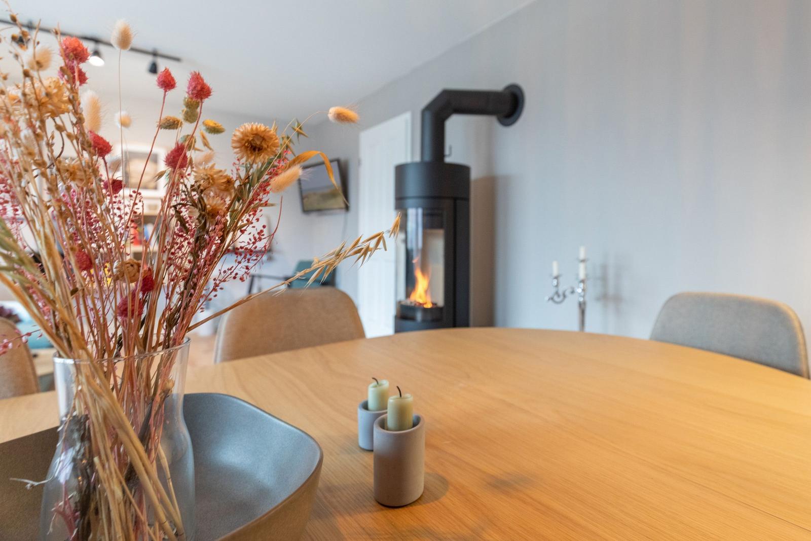 Runder Tisch mit Kerzen und Trockenblumen. Im Hintergrund steht ein Kaminofen.