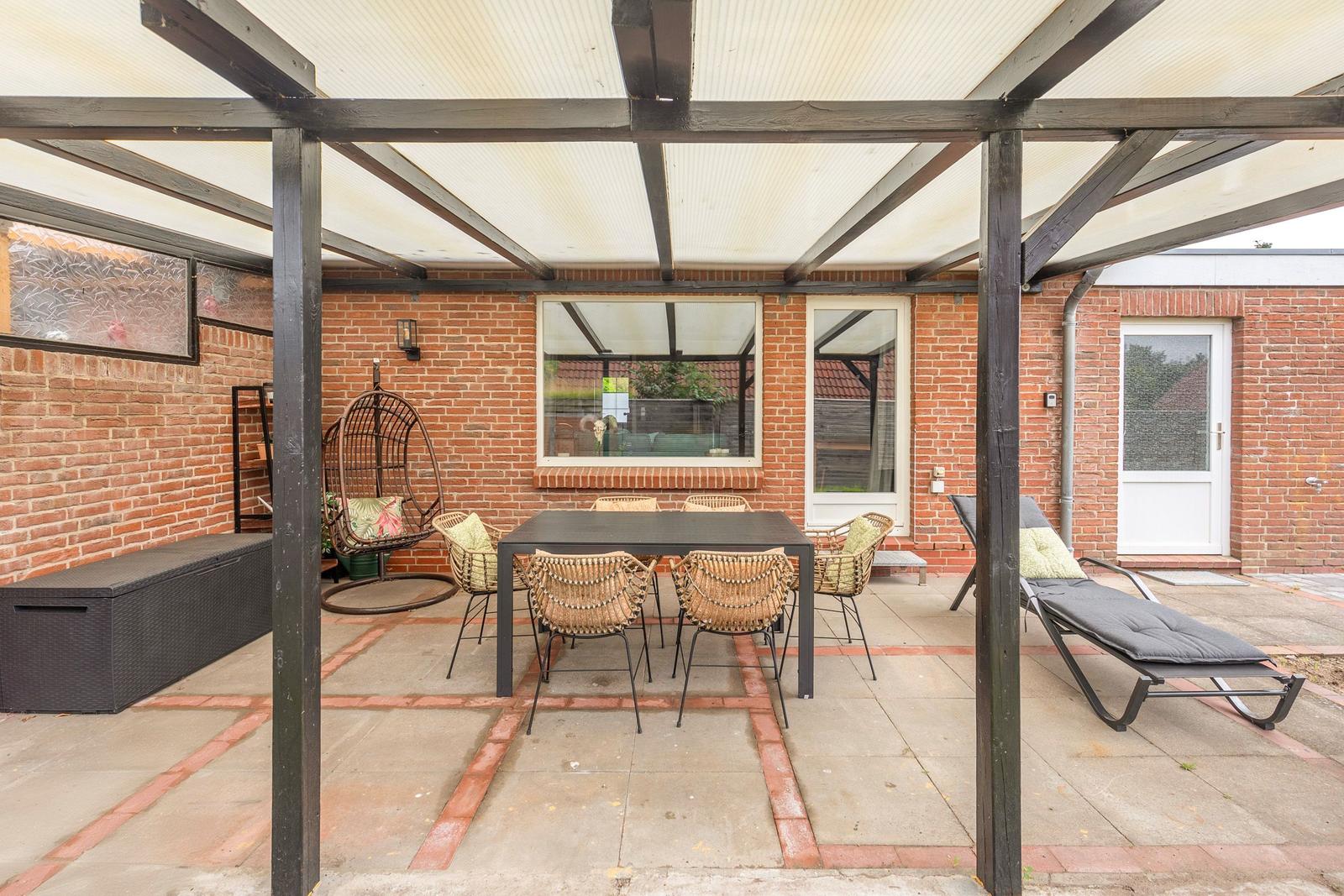 Terrasse mit Sitzgruppe, Liegestuhl und Hängesessel unter Dach.