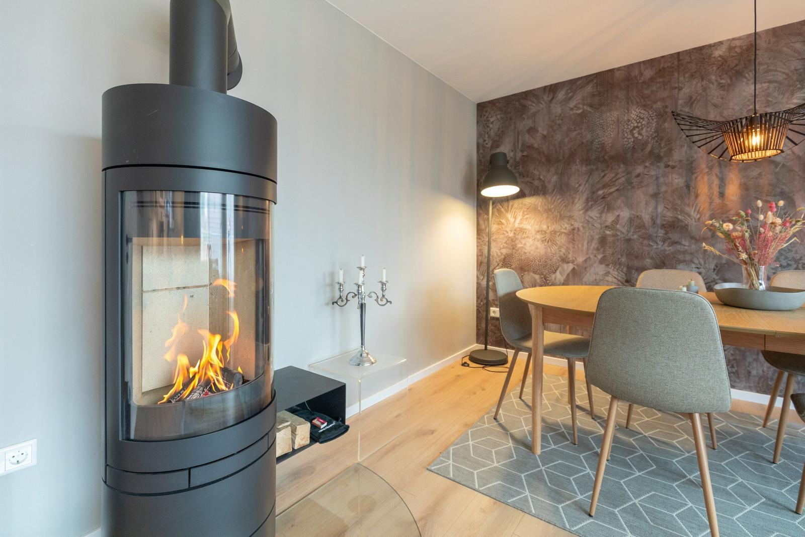 Kaminofen mit brennendem Feuer, Esstisch mit Stühlen und Wand mit Muster.