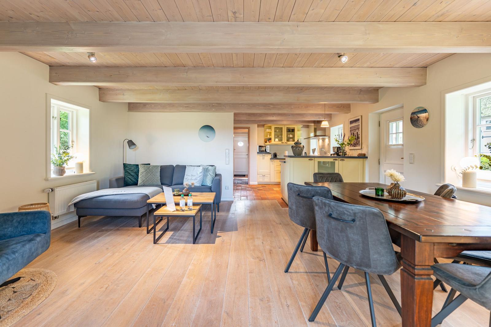 Wohn- und Essbereich mit Holzboden, Sofa, Esstisch und Küche im Hintergrund.