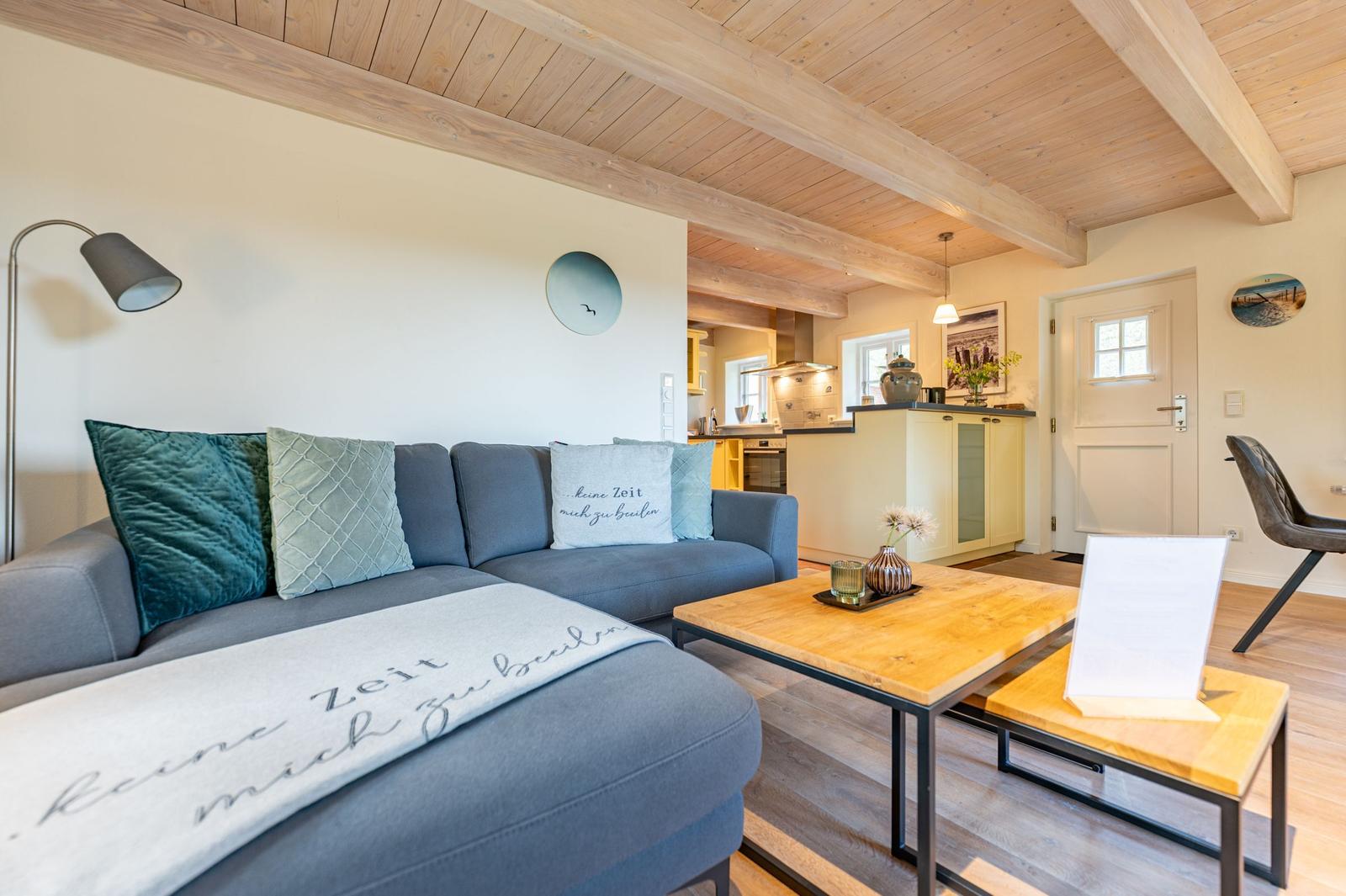 Wohnzimmer mit Sofa, Couchtisch und Küchenbereich unter Holzdecke.