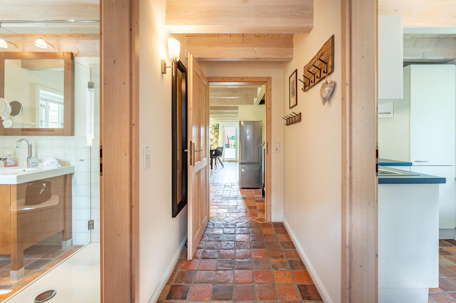 Flur mit Terrakottboden, Küche und Bad sichtbar. Holzdecken und Wanddekoration.
