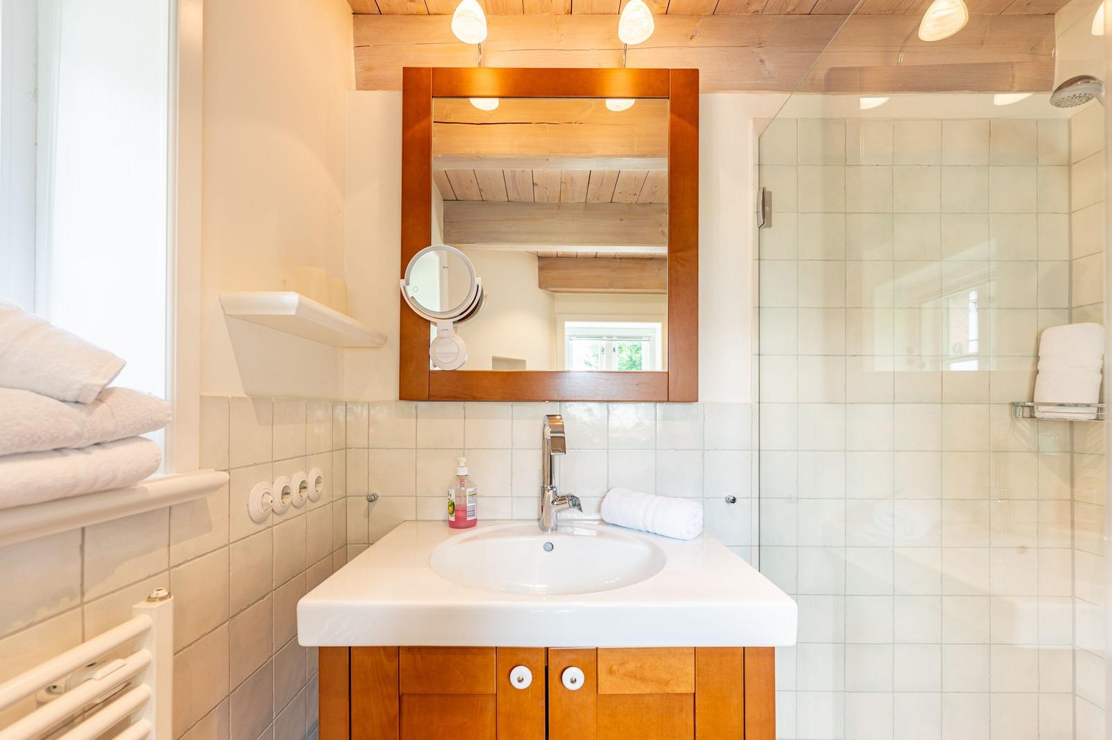 Badezimmer mit Waschbecken, Spiegel und Dusche. Holzdecke und weiße Fliesen.
