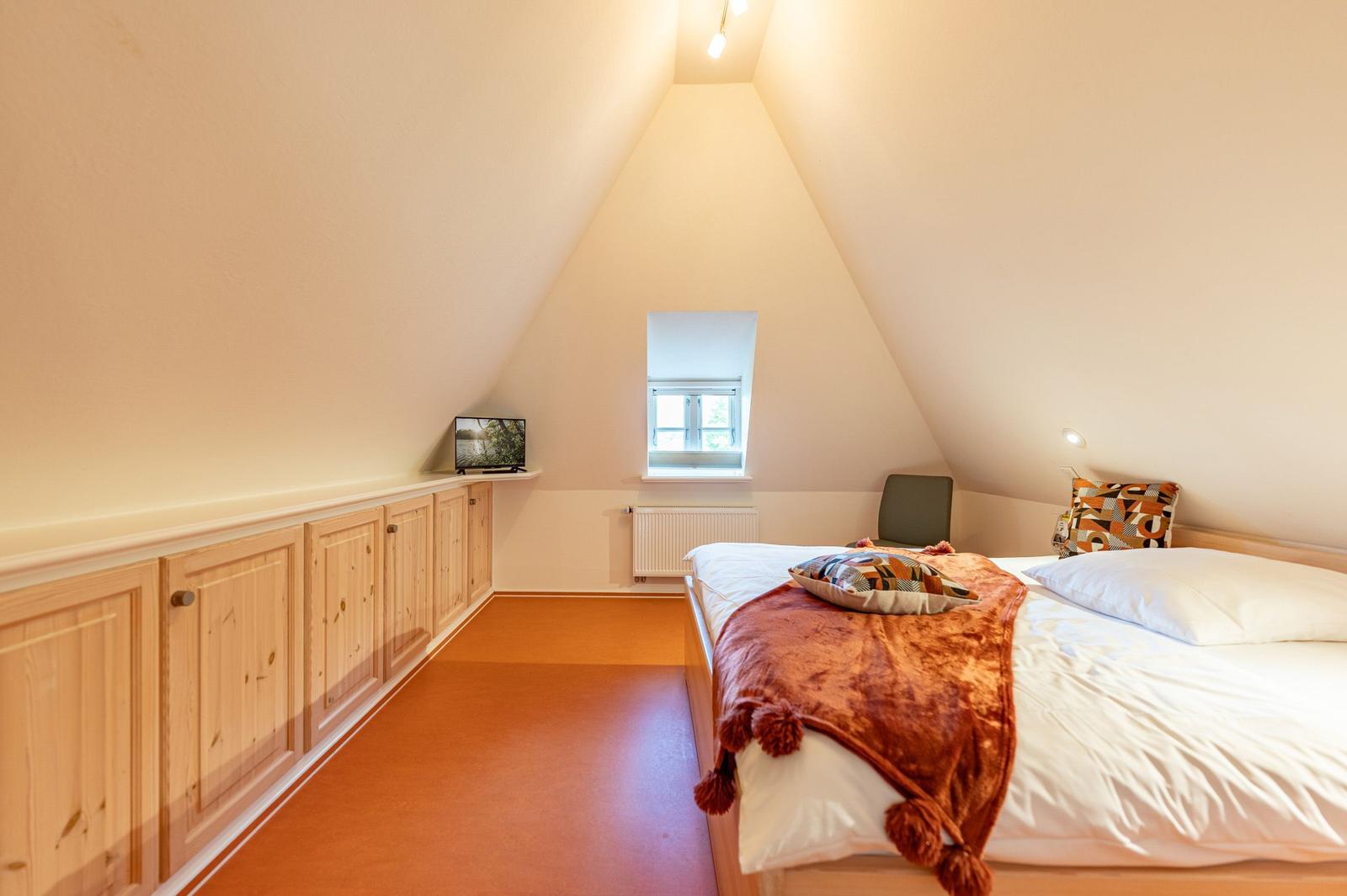 Schlafzimmer mit Dachschrägen, Bett, Fenster und Holzschränken.