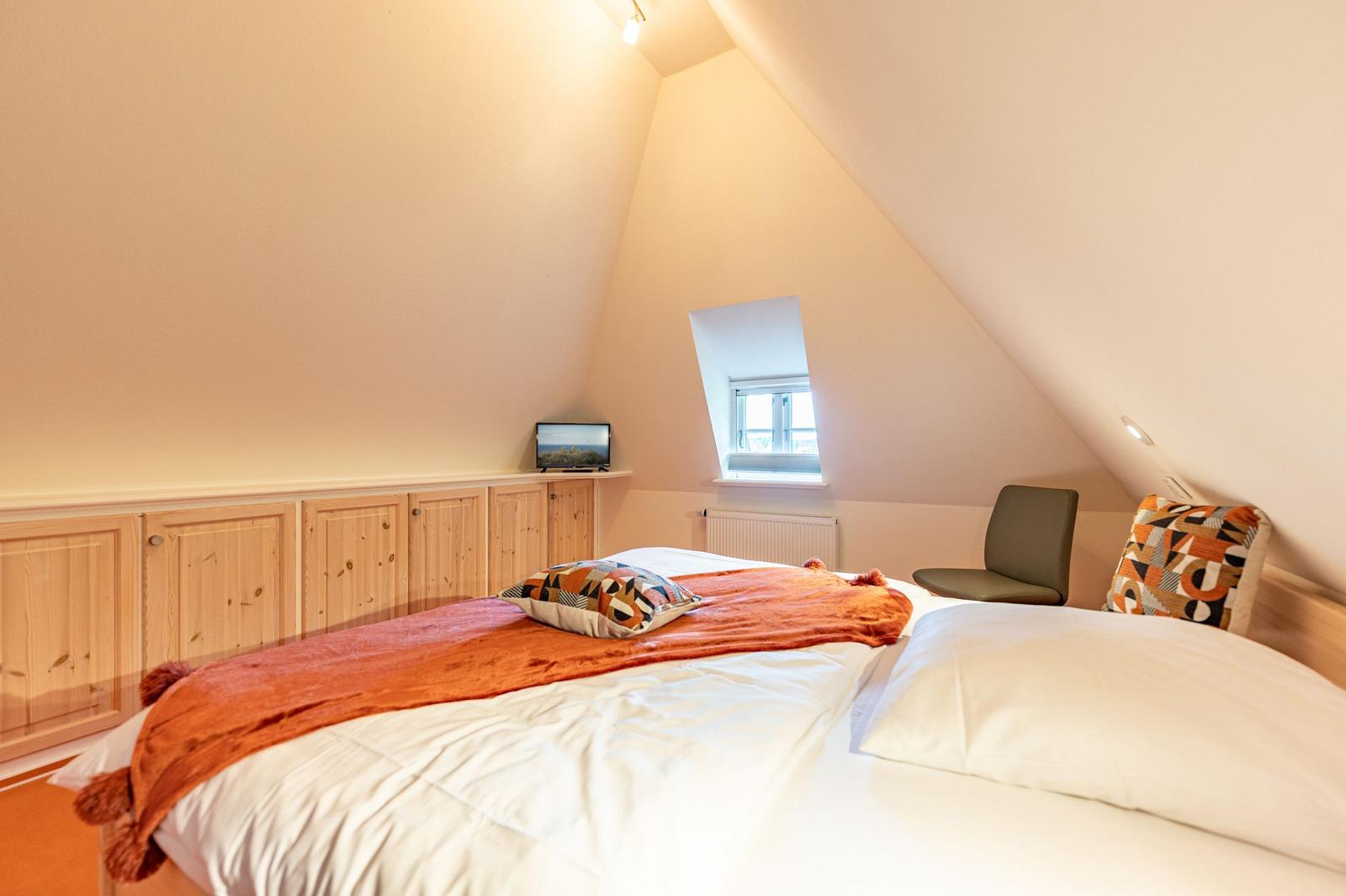 Dachgeschosszimmer mit Bett, Fenster und Holzschränken.