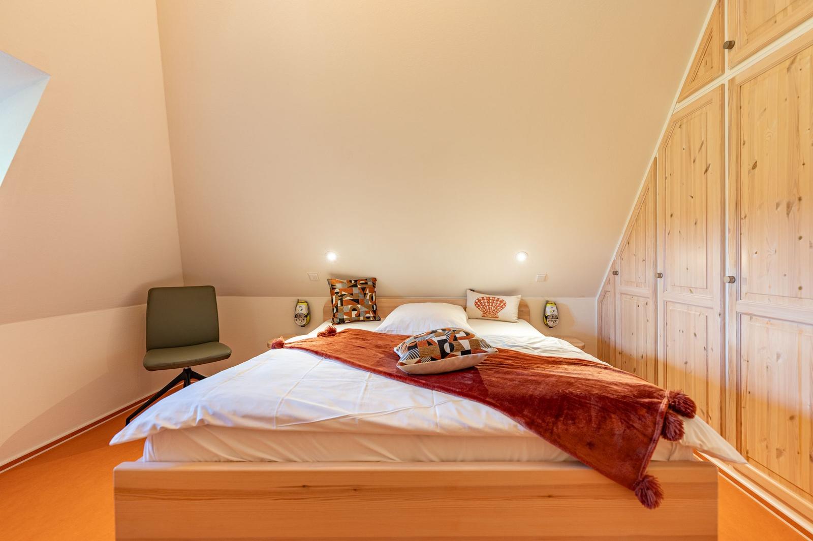 Schlafzimmer mit Bett, Holzschrank und Stuhl unter schrägen Decken.