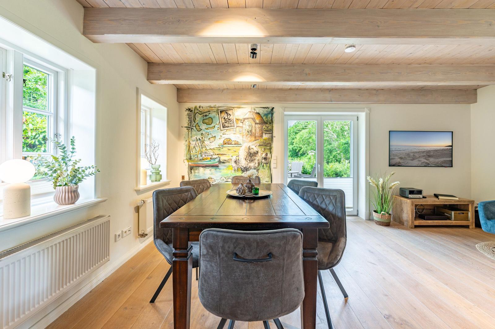 Esszimmer mit Holzdecke, Tisch und Stühlen, Wandbild und Fenster zum Garten.