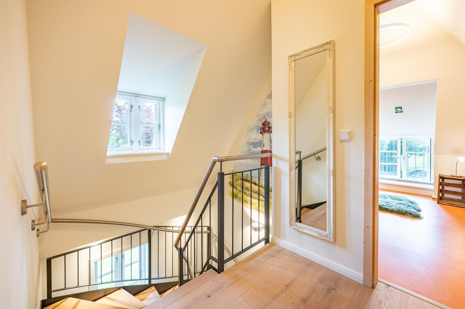 Treppe mit Metallgeländer führt zum Obergeschoss. An der Wand hängt ein großer Spiegel.