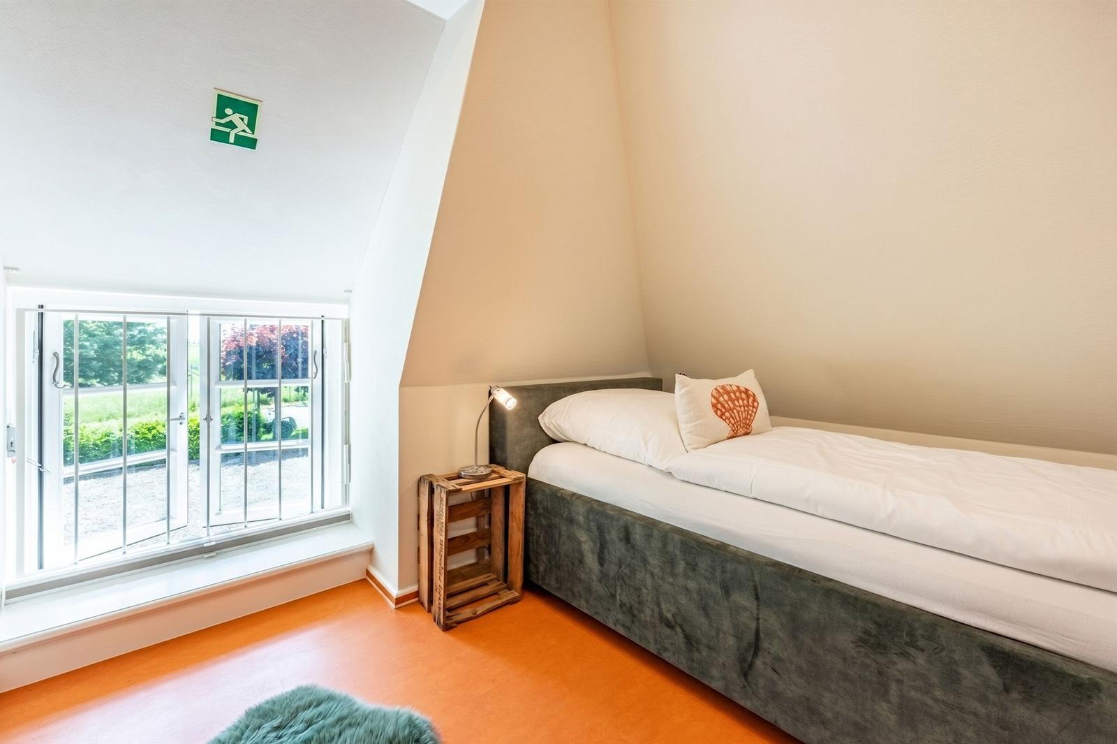 Ein Schlafzimmer mit Bett, Nachttisch und Fenster. Der Boden ist orange.