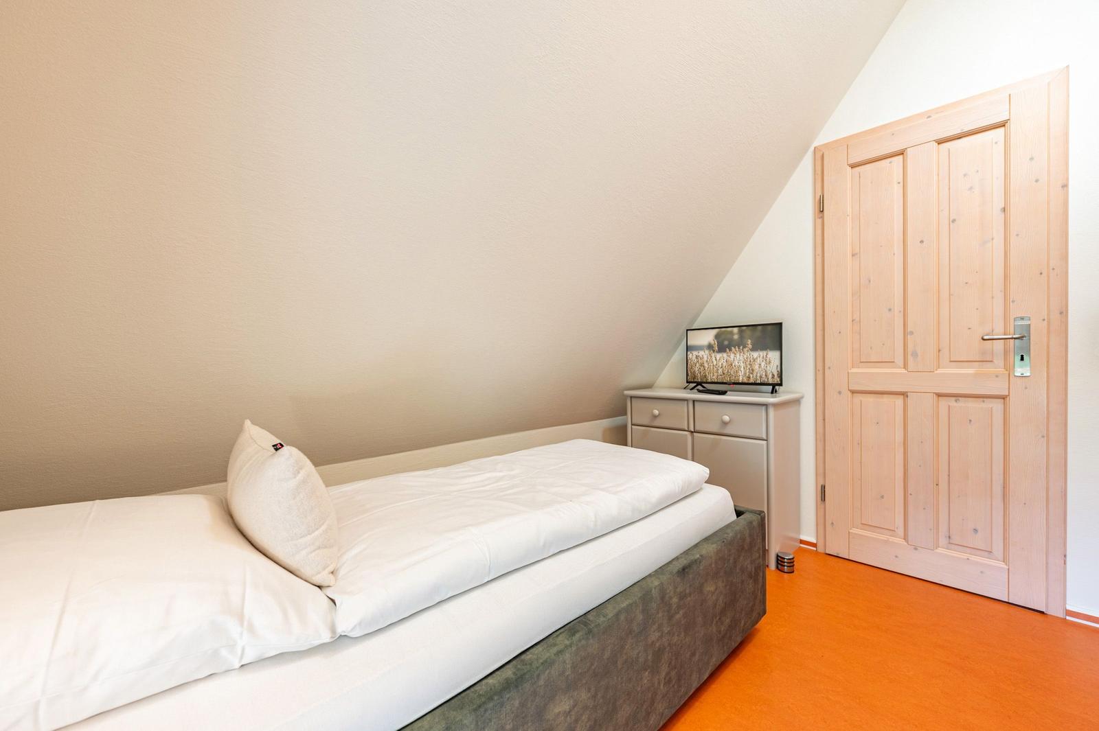Schlafzimmer mit Bett, Schrank und Fernseher unter Dachschräge
