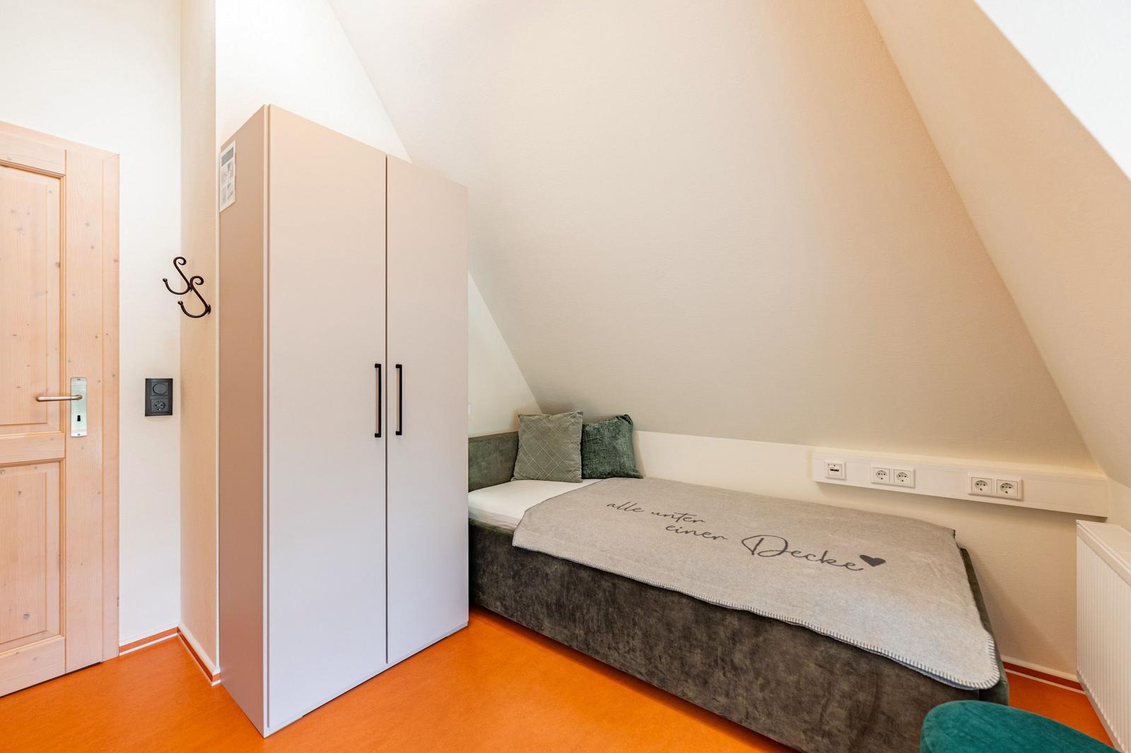 Schlafzimmer mit Dachschrägen, Bett, Kleiderschrank und Tür.
