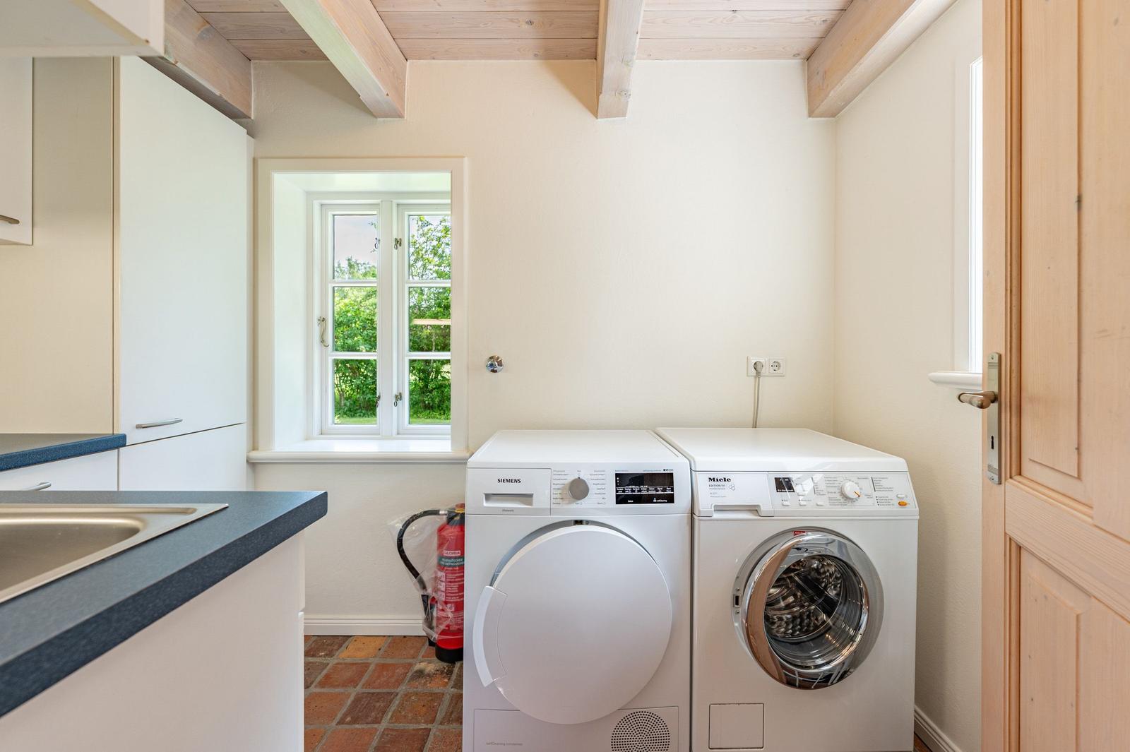 Wäschetrockner und Waschmaschine in der Waschküche mit Fenster und Holzbalken.