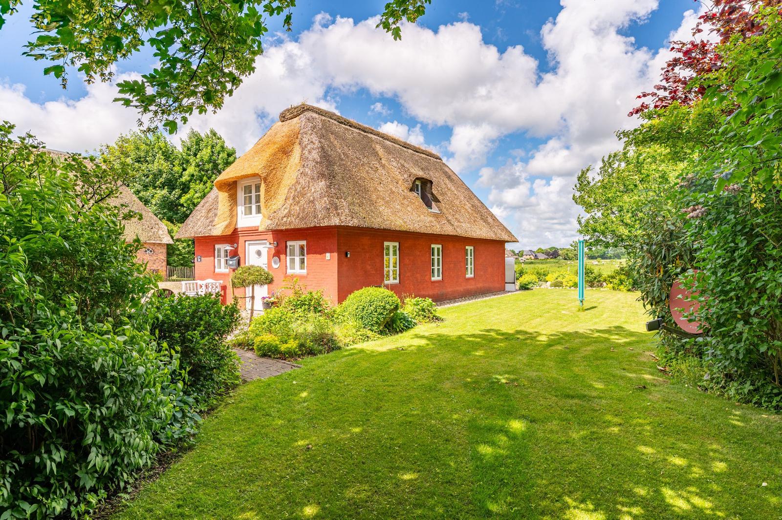 Rotes Haus mit Strohdach und grünem Garten unter blauem Himmel.
