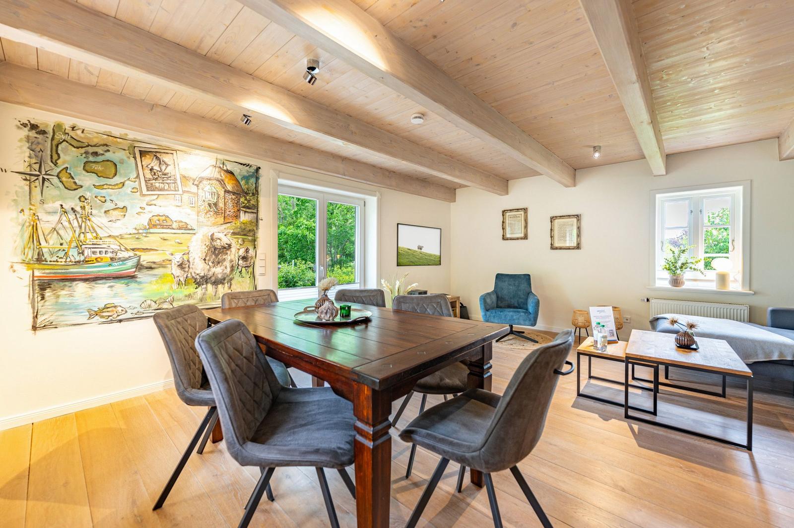 Esszimmer mit Holztisch, Stühlen und Wandgemälde. Wohnbereich mit Sofa und Tisch.