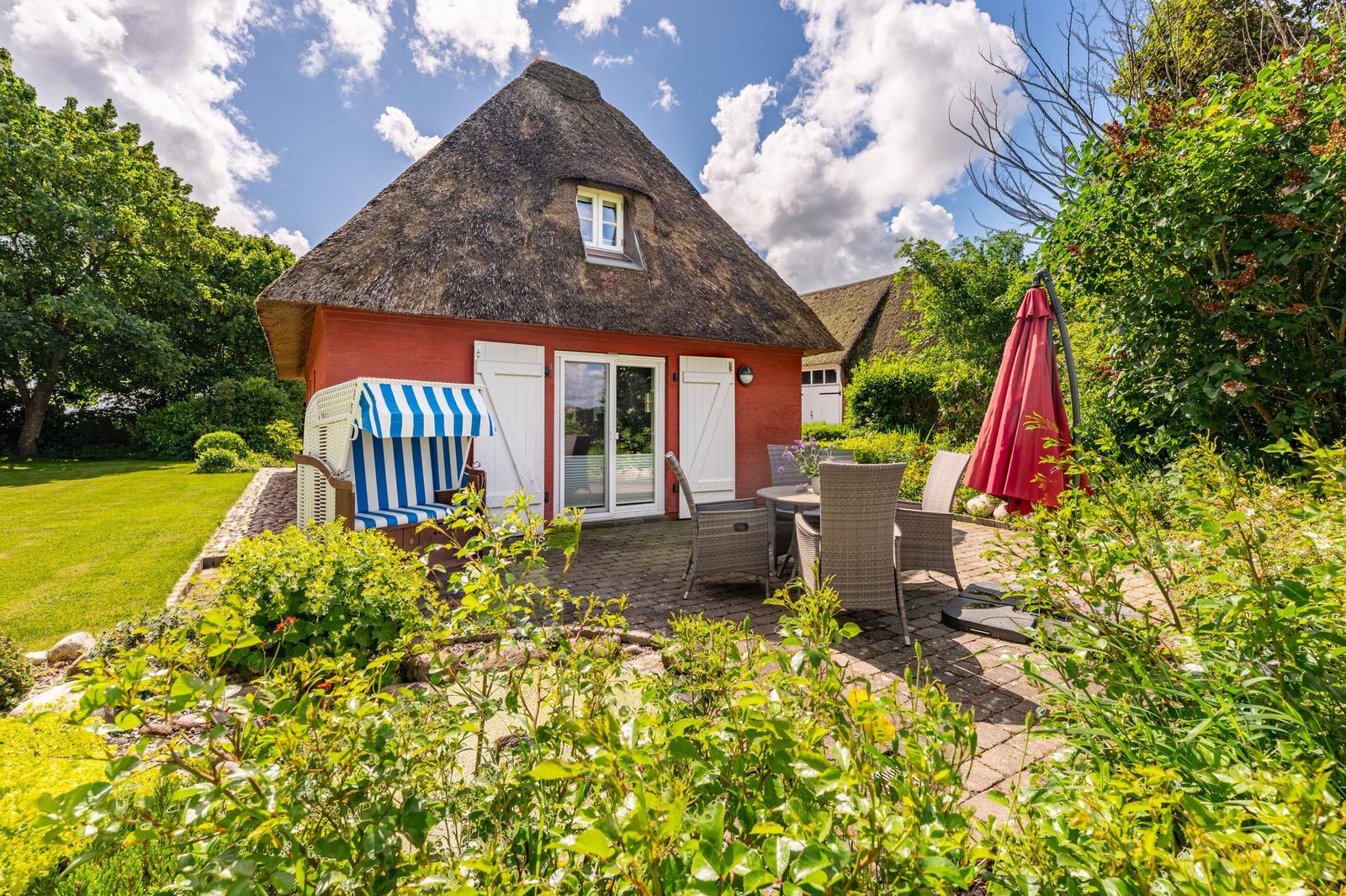 Rotes Haus mit Strohdach, Terrasse mit Gartenmöbeln und Strandkorb.