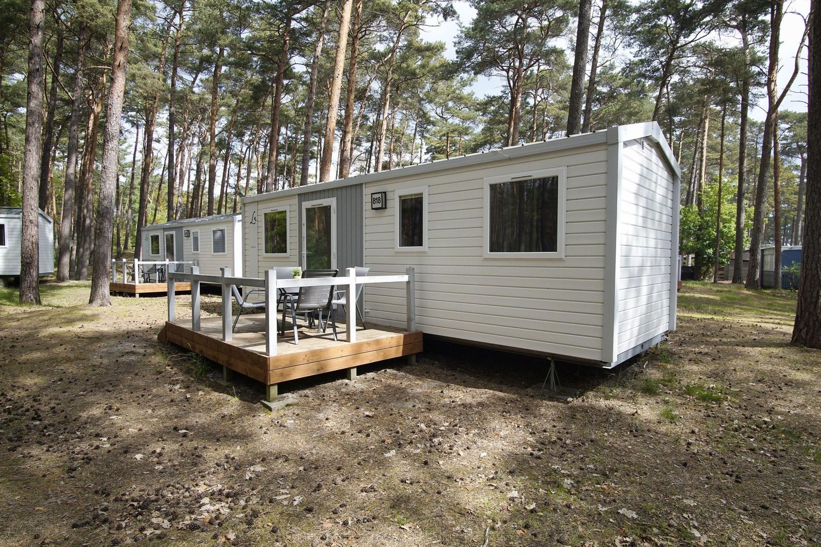 Wohnwagen mit Terrasse im Wald. Holzterrasse mit Tisch und Stühlen.