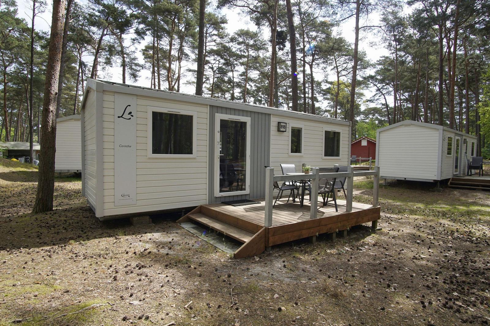Wohnwagen mit Terrasse im Wald. Holzterrasse mit Tisch und Stühlen.