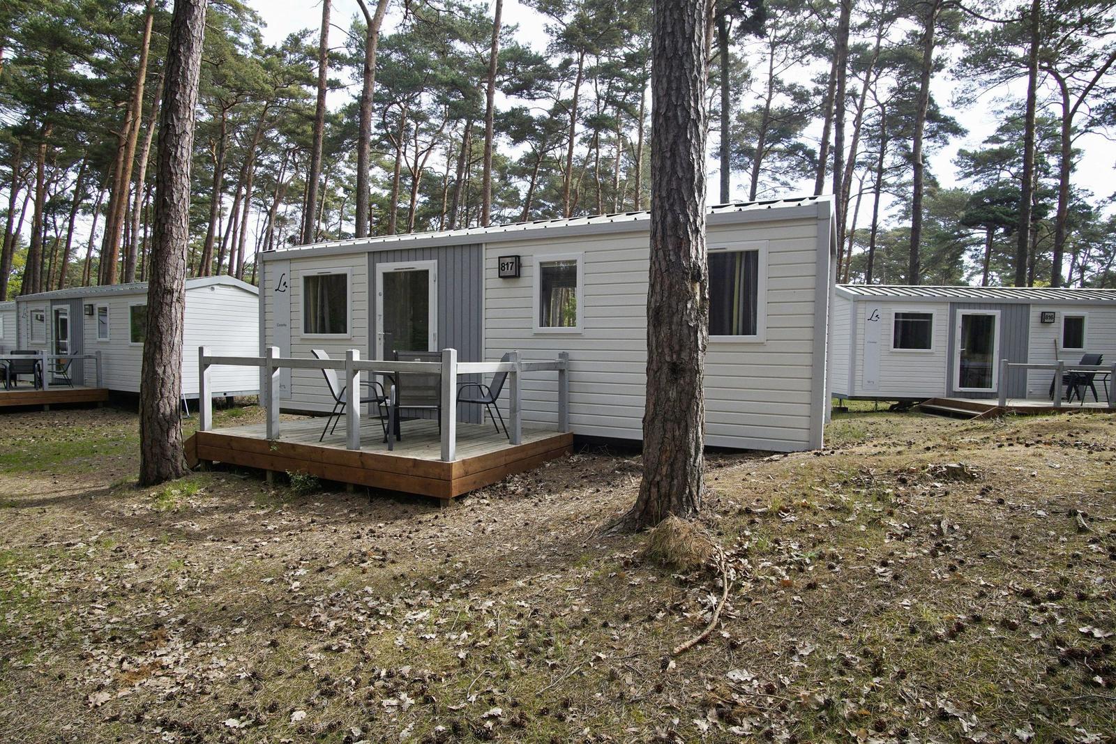 Wohnwagen mit Terrasse im Wald. Holzdecke, Stühle und Tische sind vorhanden.