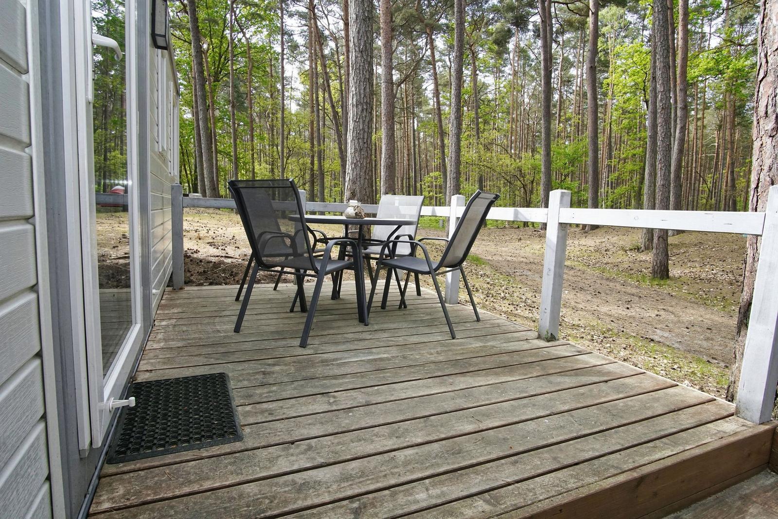 Terrasse mit Tisch und Stühlen im Wald. Holzdeck und weißer Zaun.