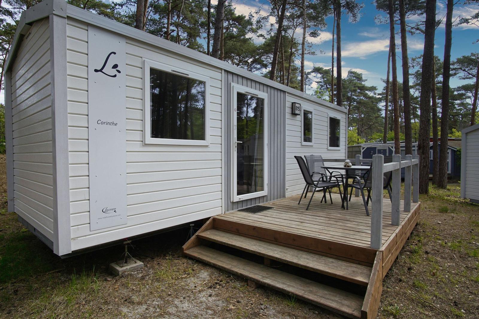 Wohnwagen mit Terrasse und Sitzgruppe im Wald. Holzterrasse mit Tisch und Stühlen.