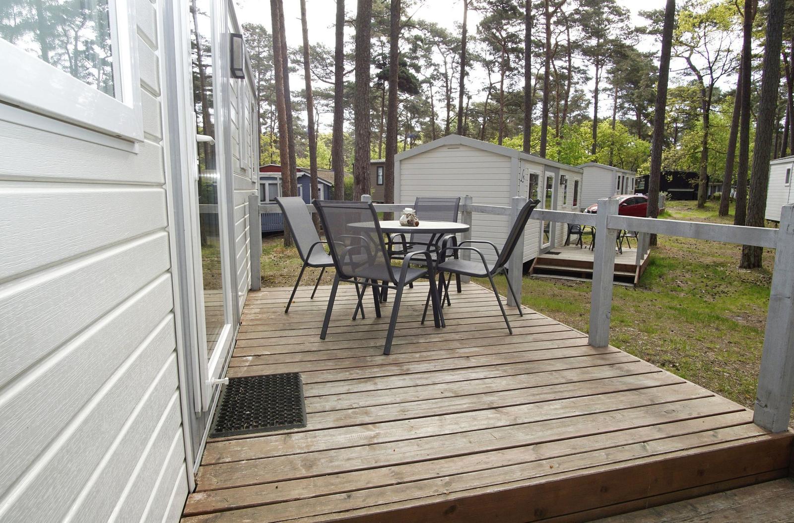 Terrasse mit Tisch und Stühlen vor einem weißen Ferienhaus im Wald.