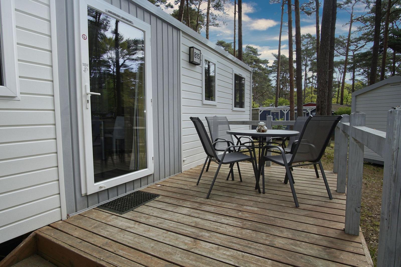 Terrasse mit Tisch und Stühlen vor einem Ferienhaus in einem Wald.