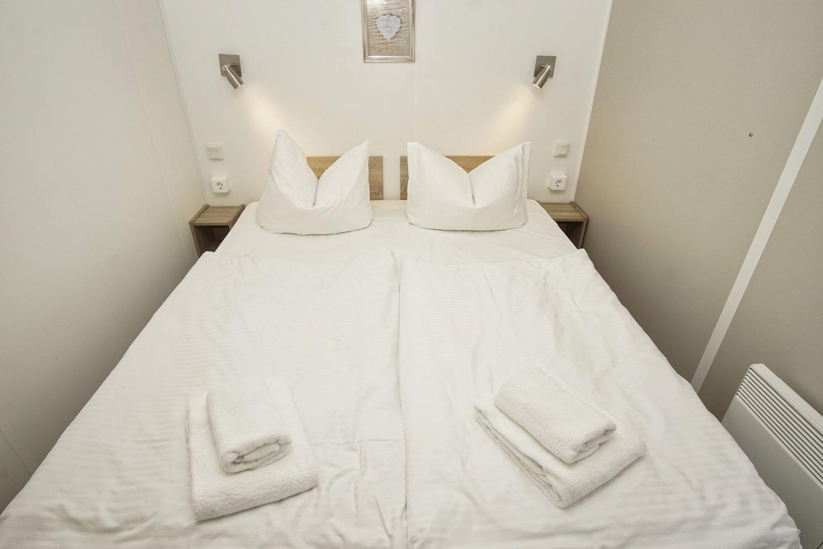 Doppelbett mit weißen Laken, zwei Kissen und gefalteten Handtüchern.