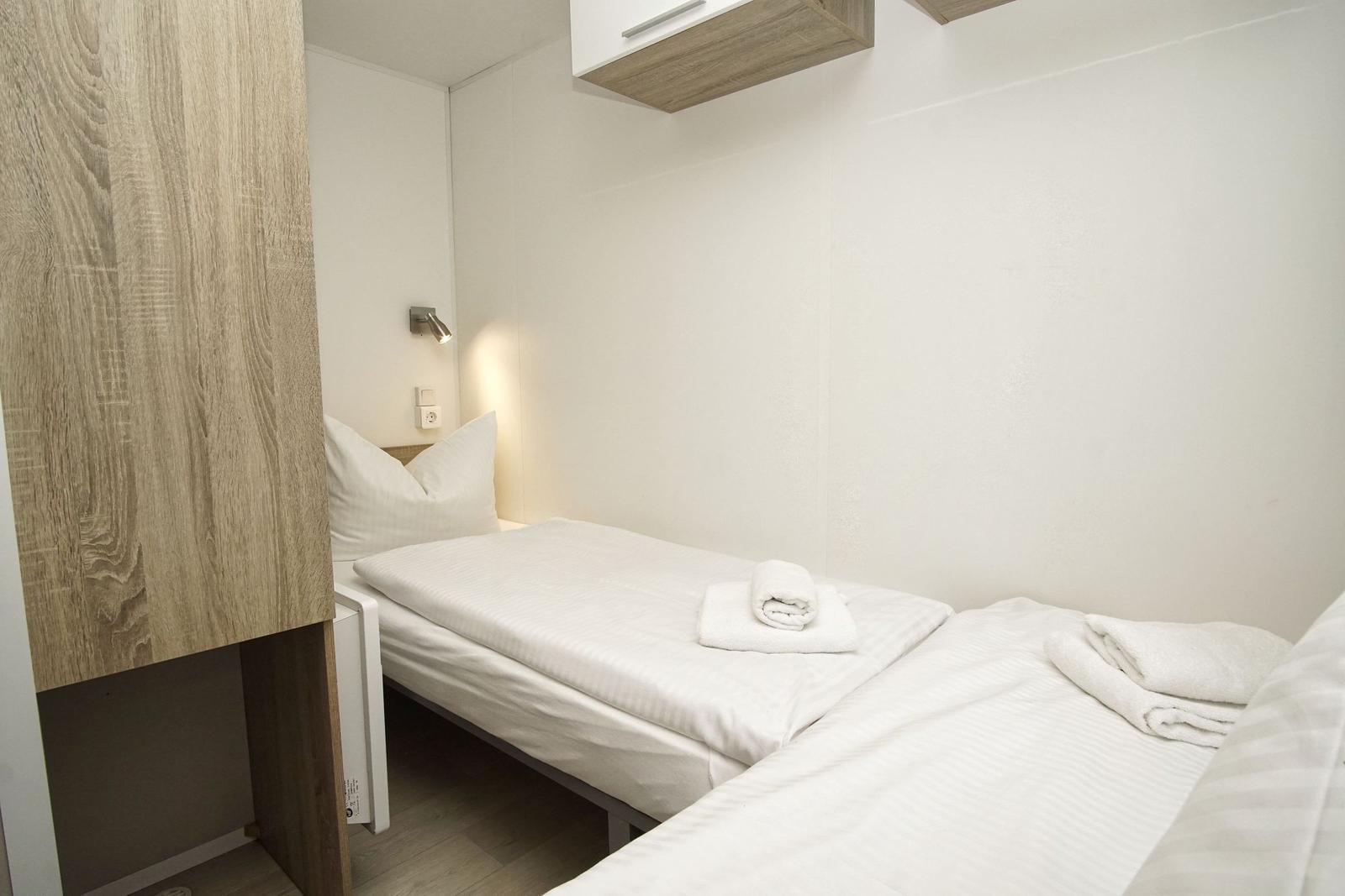 Zimmer mit einem Bett, weißen Bettwäsche und Handtüchern. Holzpaneel an der Wand.