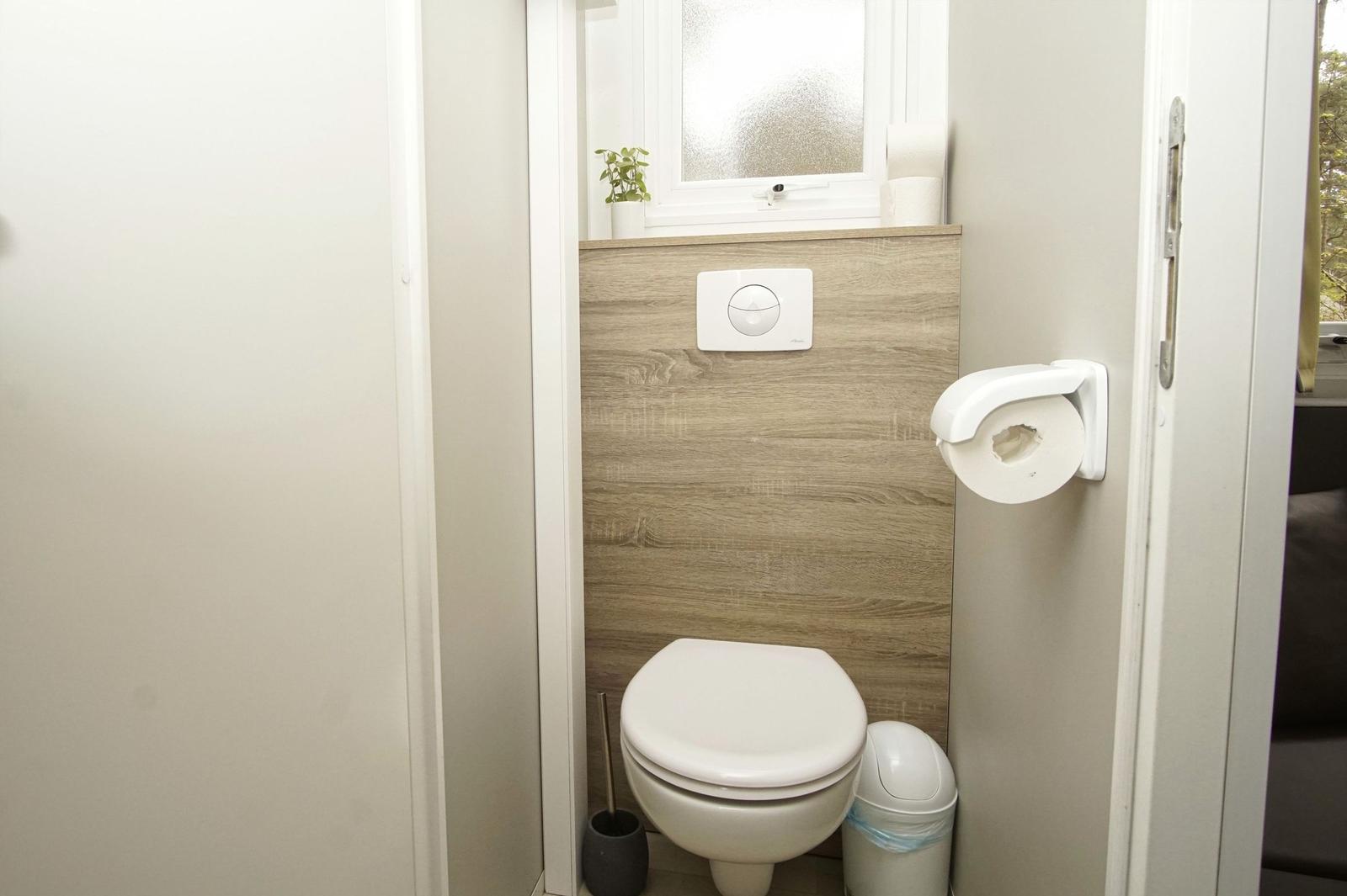 Badezimmer mit Toilette, WC-Behälter und Fenster. Auf dem Fensterbrett steht eine Pflanze.