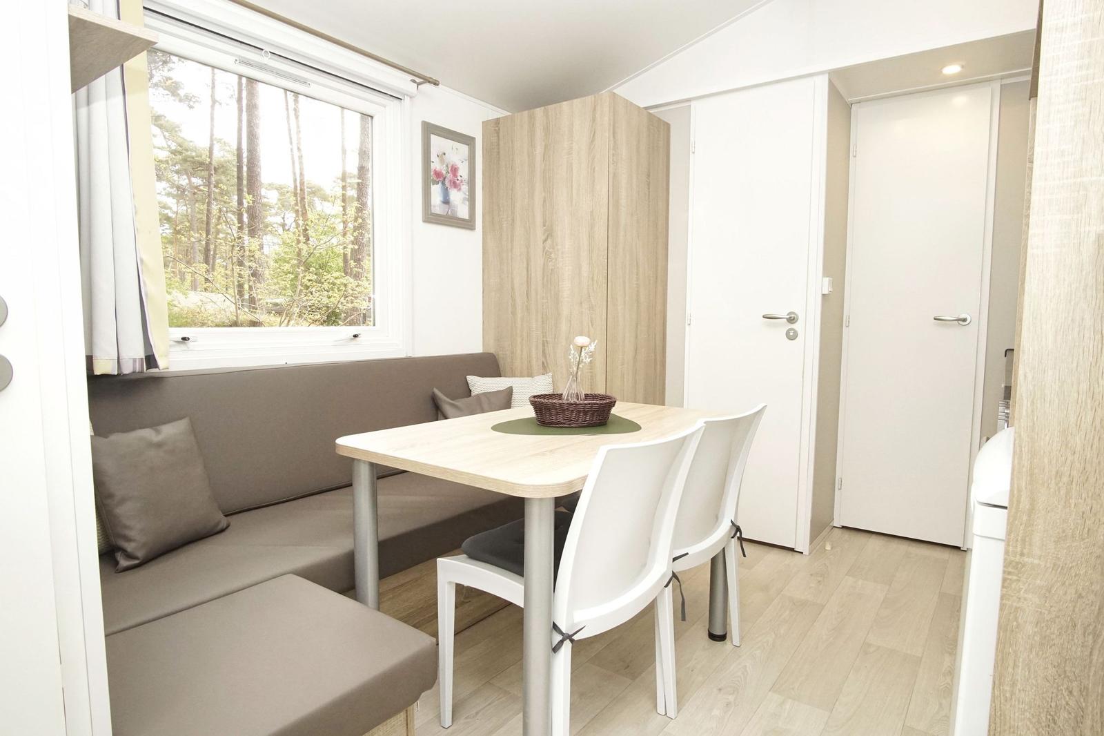 Essbereich mit Sitzbank, Tisch und Stühlen. Fenster zeigt Wald. Hintergrund: Schrank und Türen.