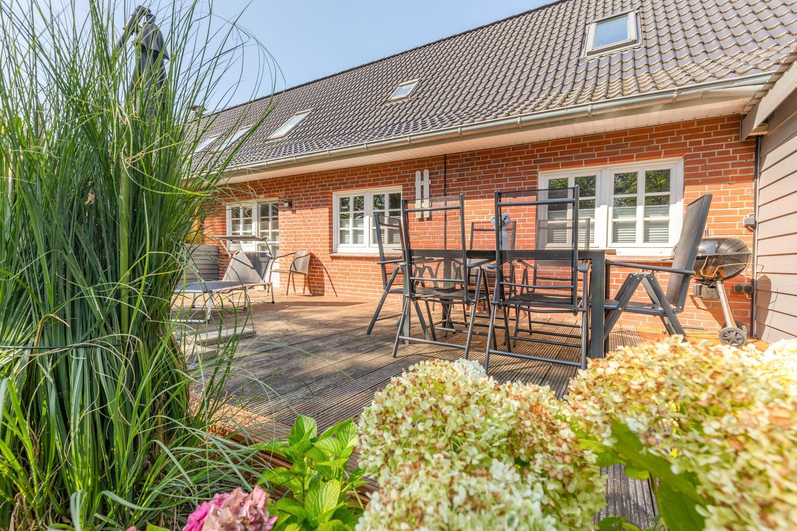 Terrasse mit Tisch, Stühlen und Grill vor einem Backsteinhaus mit Dachfenstern.
