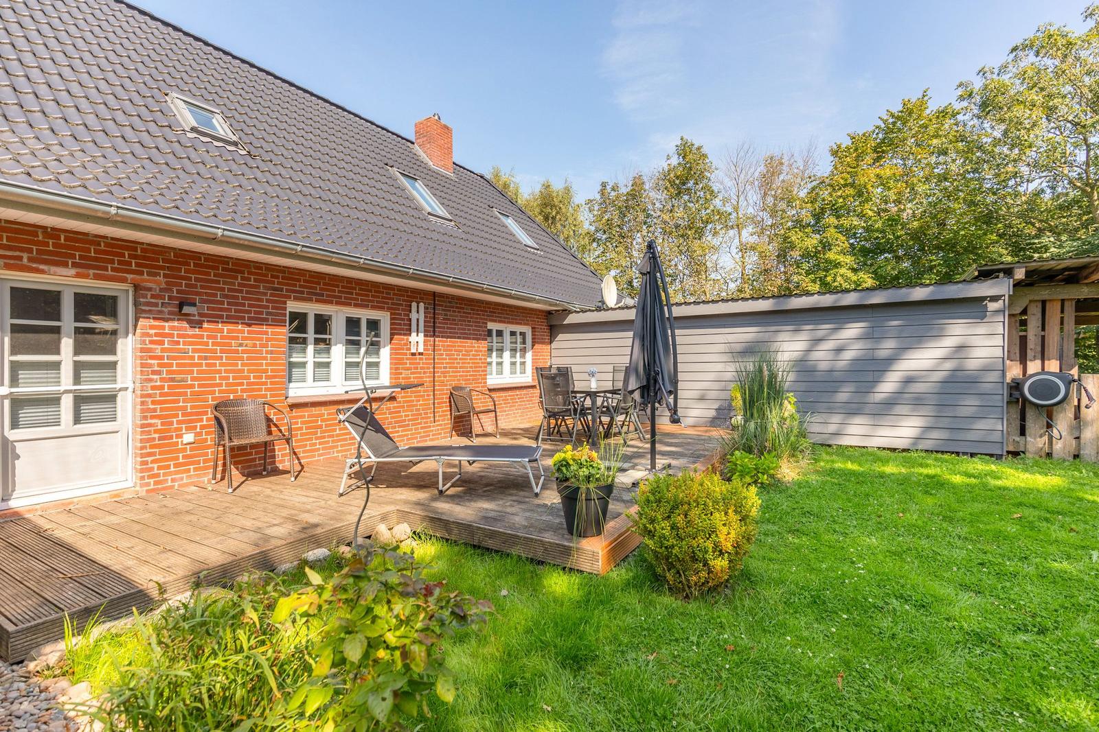 Roter Backsteinhaus mit Terrasse, Garten und Sonnenliege. Hinterhof mit Tisch und Stühlen.