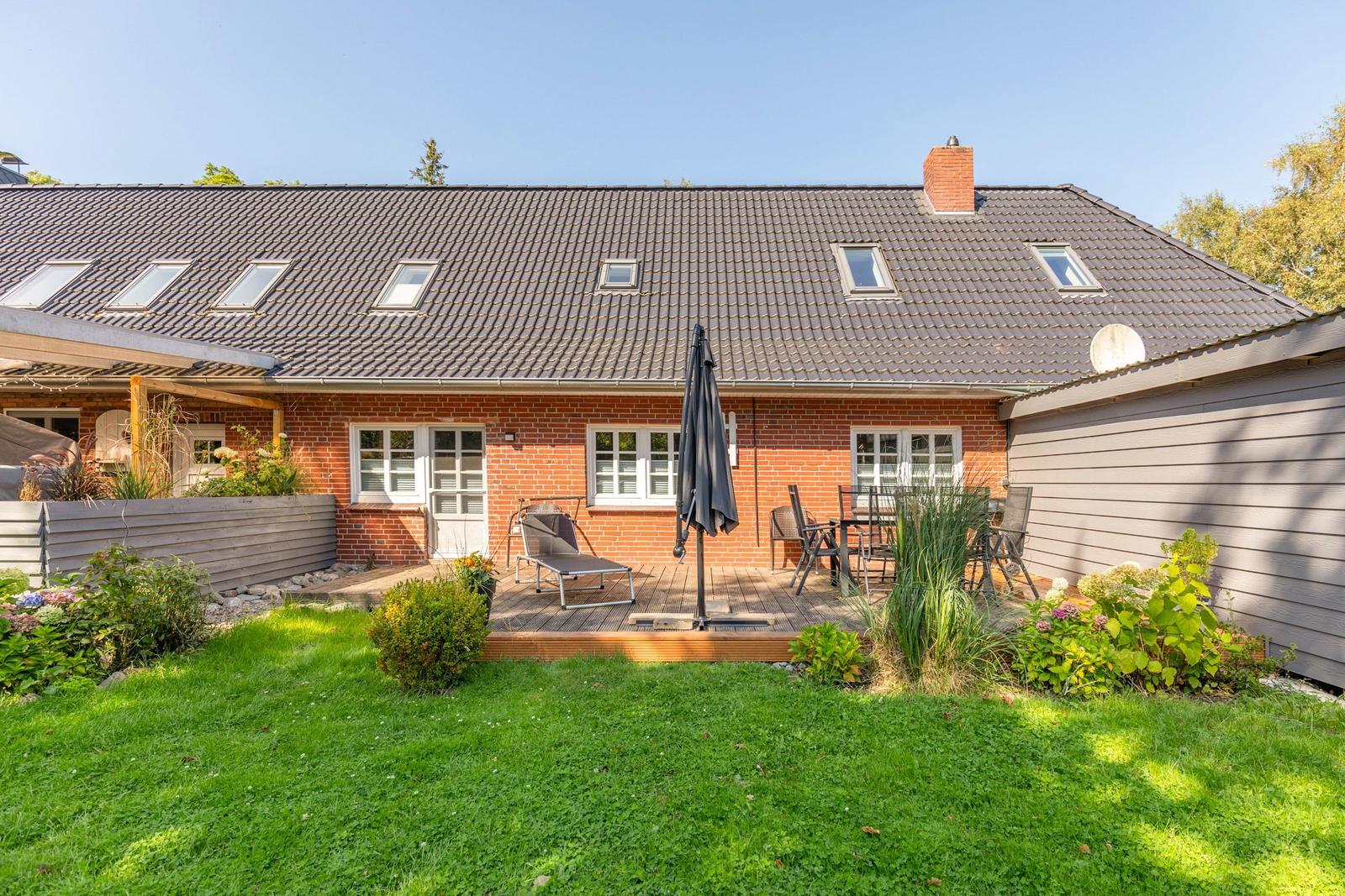 Rotes Backsteingebäude mit Terrasse, Garten und Sitzgelegenheiten.