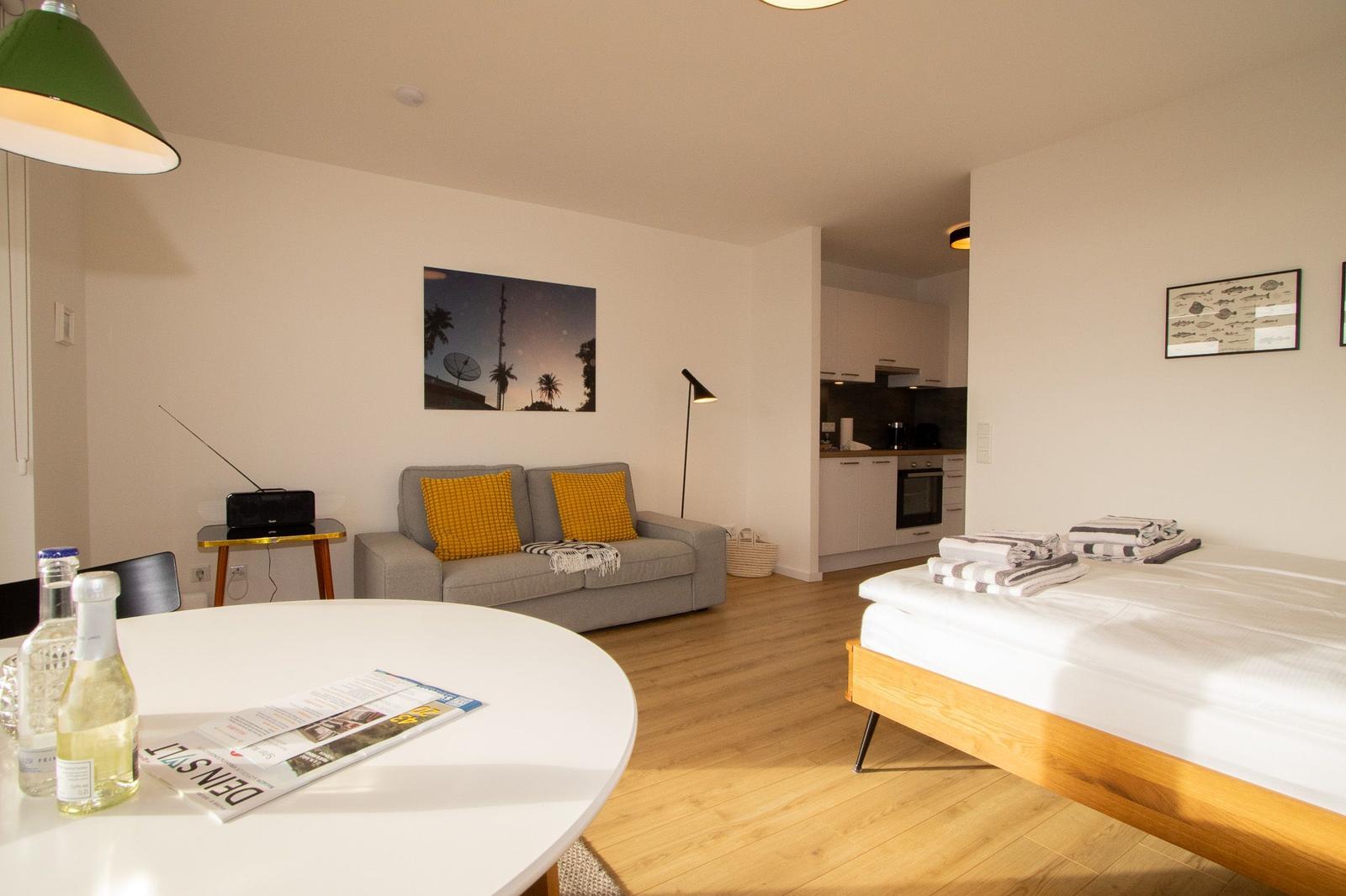 Ein Schlafzimmer mit Bett, Wohnbereich mit Sofa und Küche im Hintergrund.