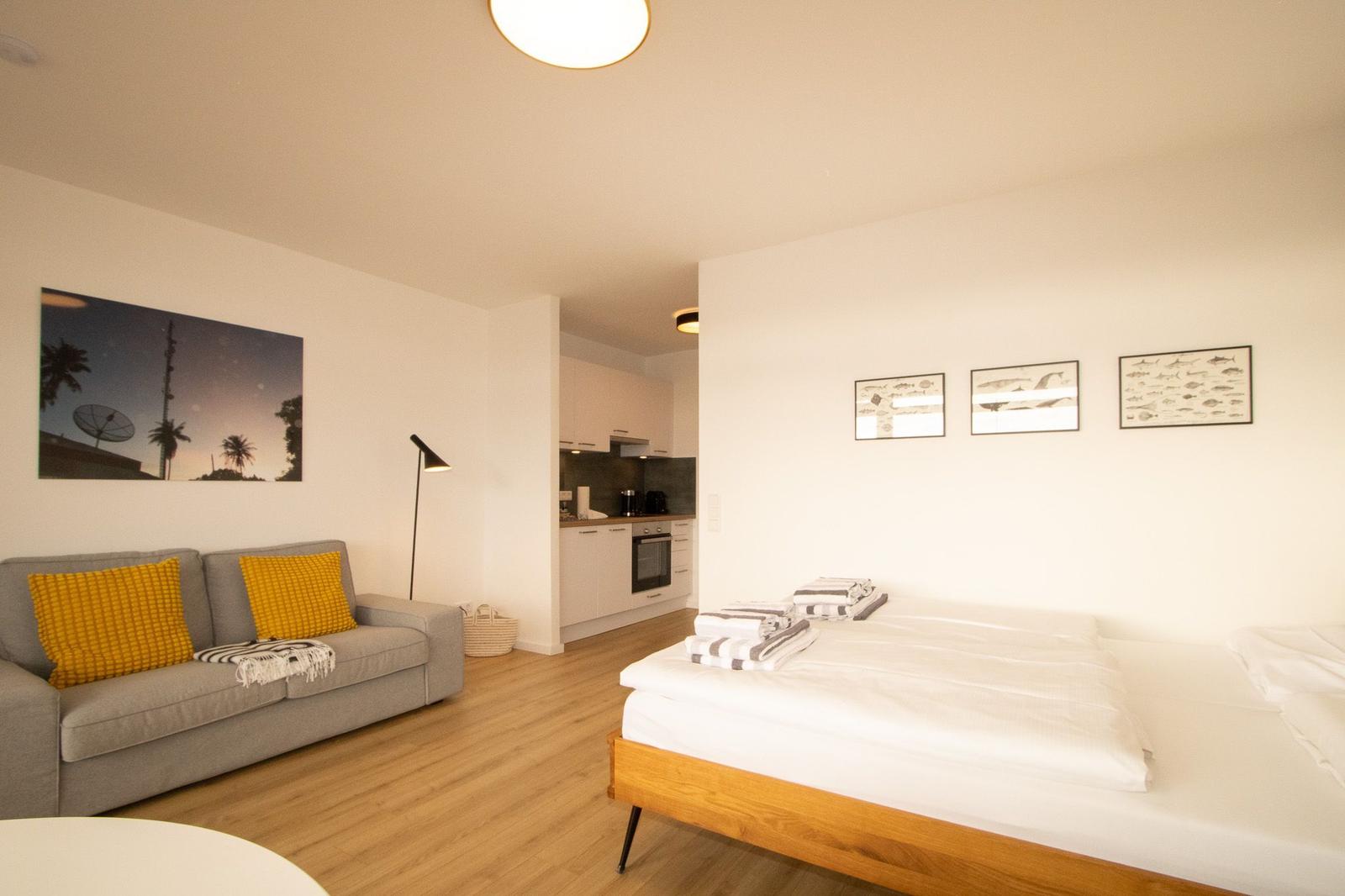 Ein Schlafzimmer mit Bett, Sofa und Küchenbereich. Wände mit Bildern und Holzboden.
