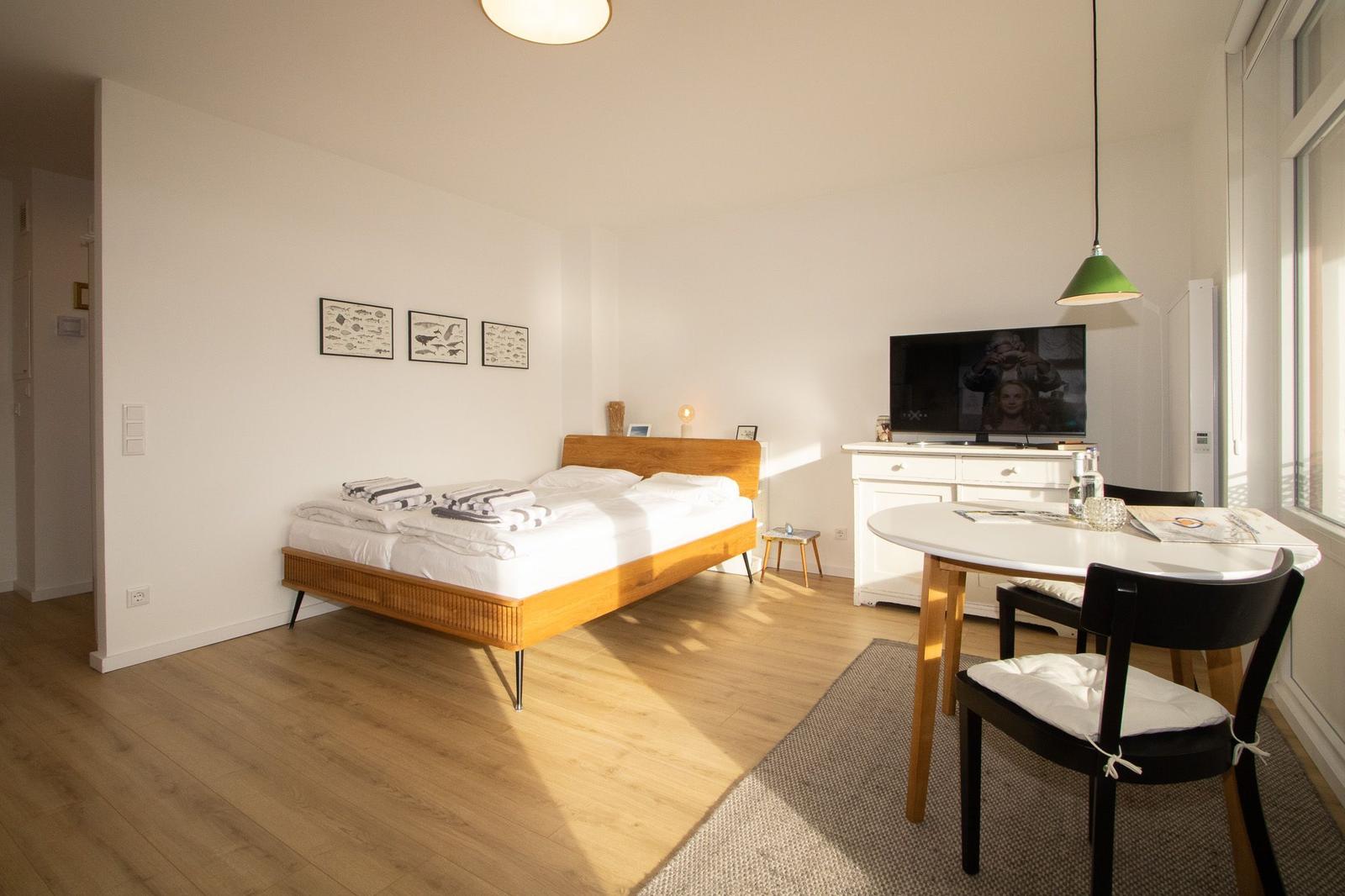 Schlafzimmer mit Bett, Esstisch und Fernseher an der Wand.