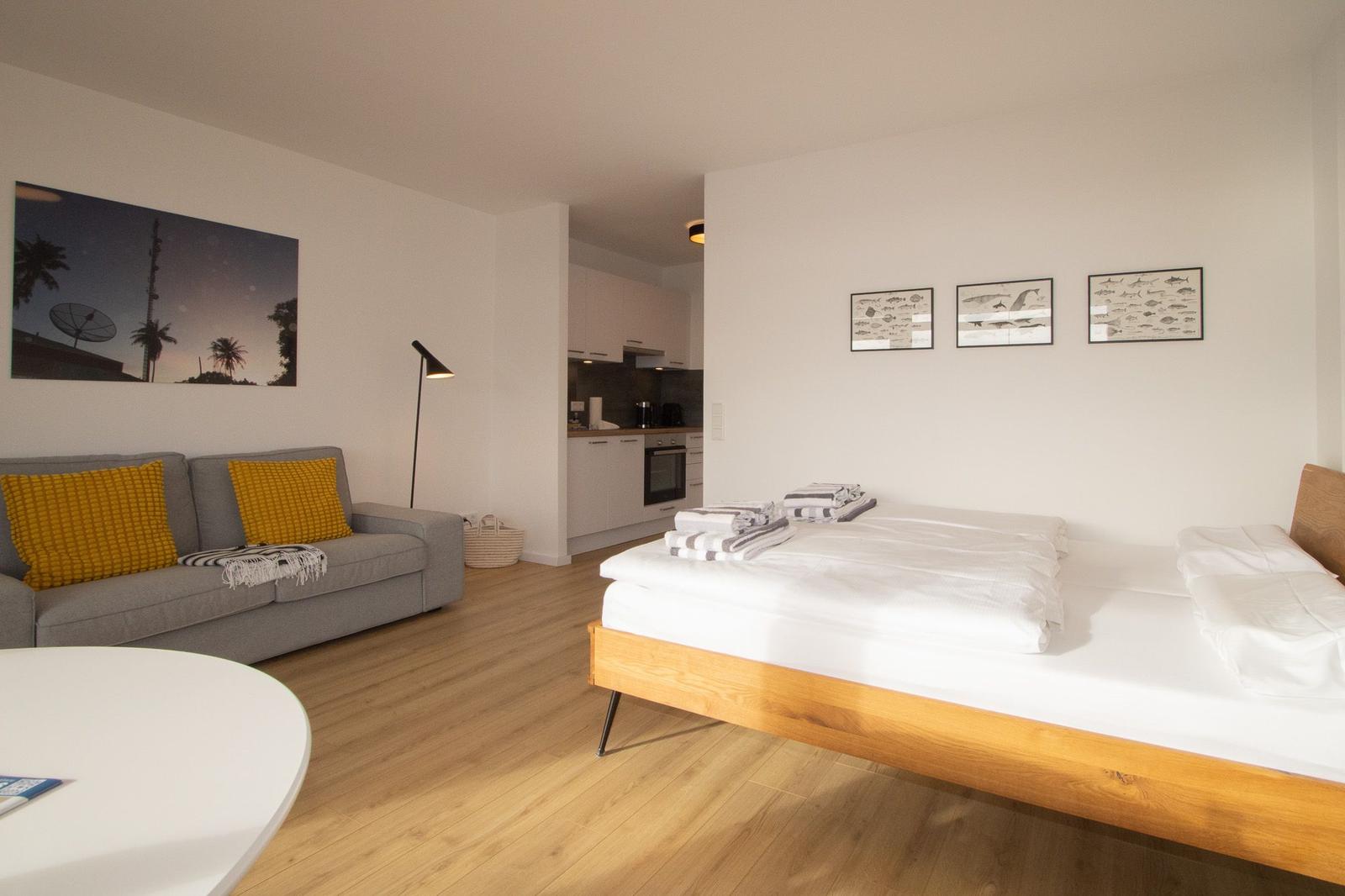 Schlafzimmer mit Bett, Sofa und Küchenbereich. Wandbilder und Holzboden.