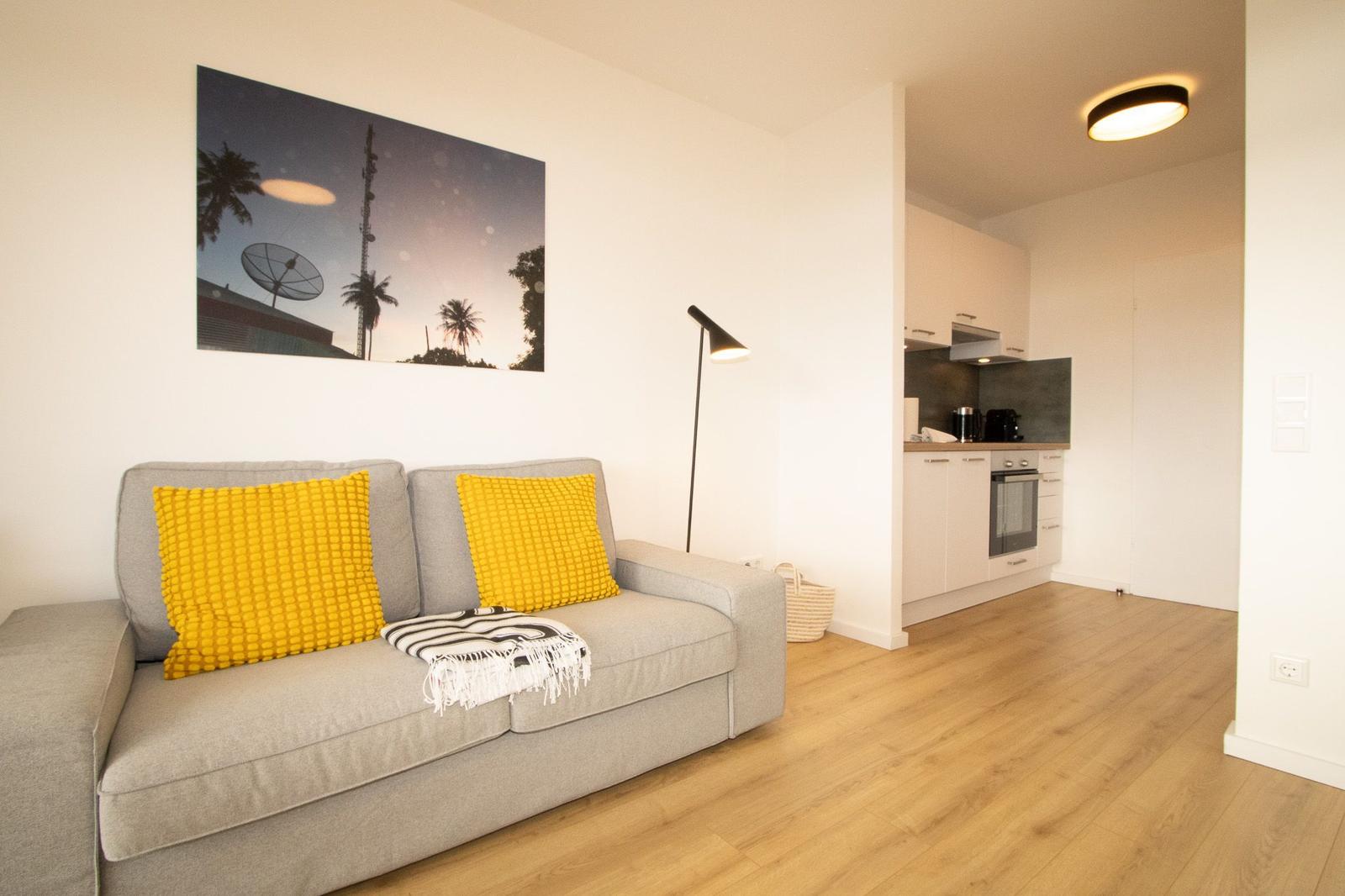 Graße Couch mit gelben Kissen, Wandbild und Küchenbereich im Hintergrund.