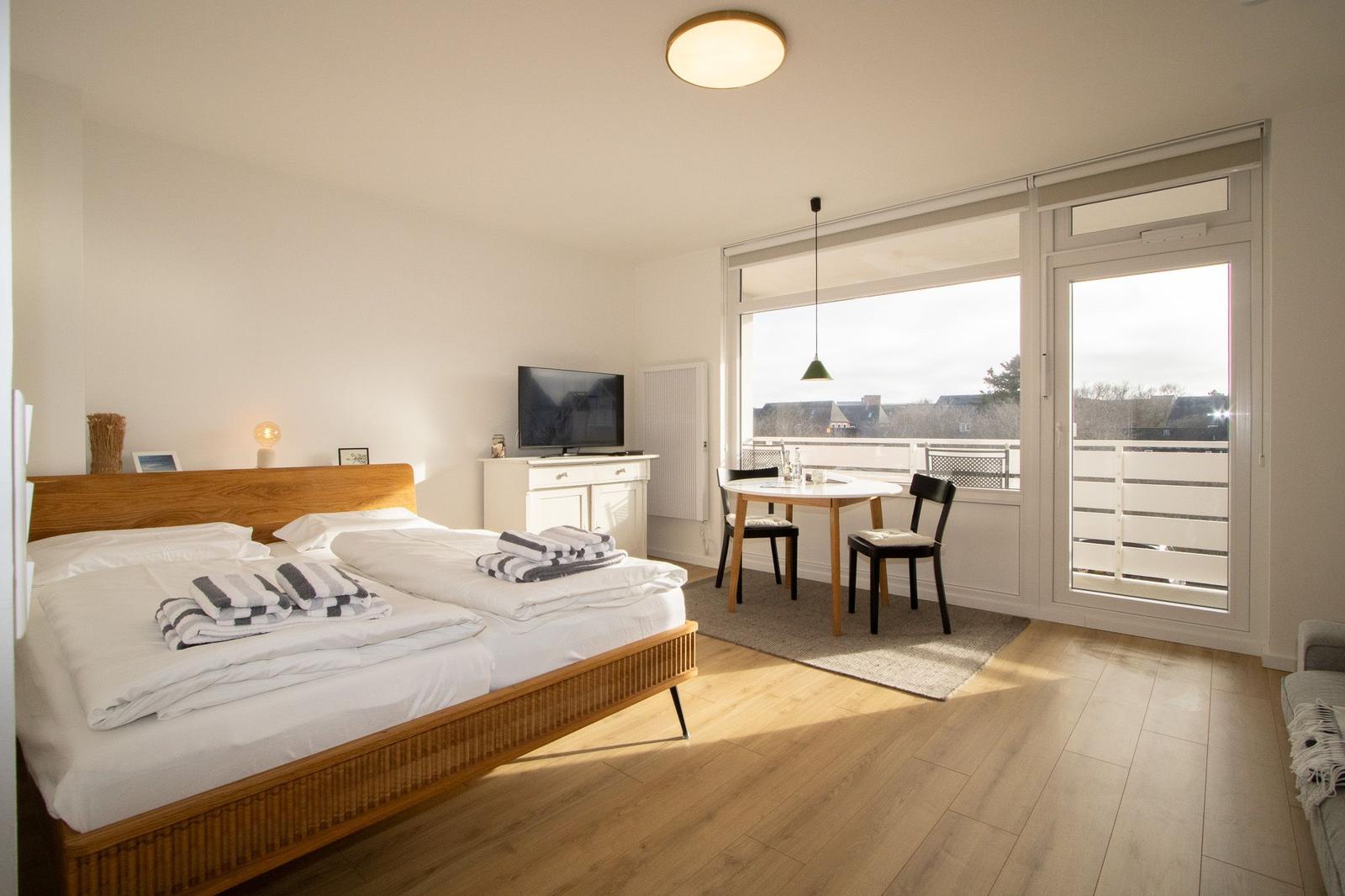 Ein Schlafzimmer mit Doppelbett, Fernseher und Balkonansicht.