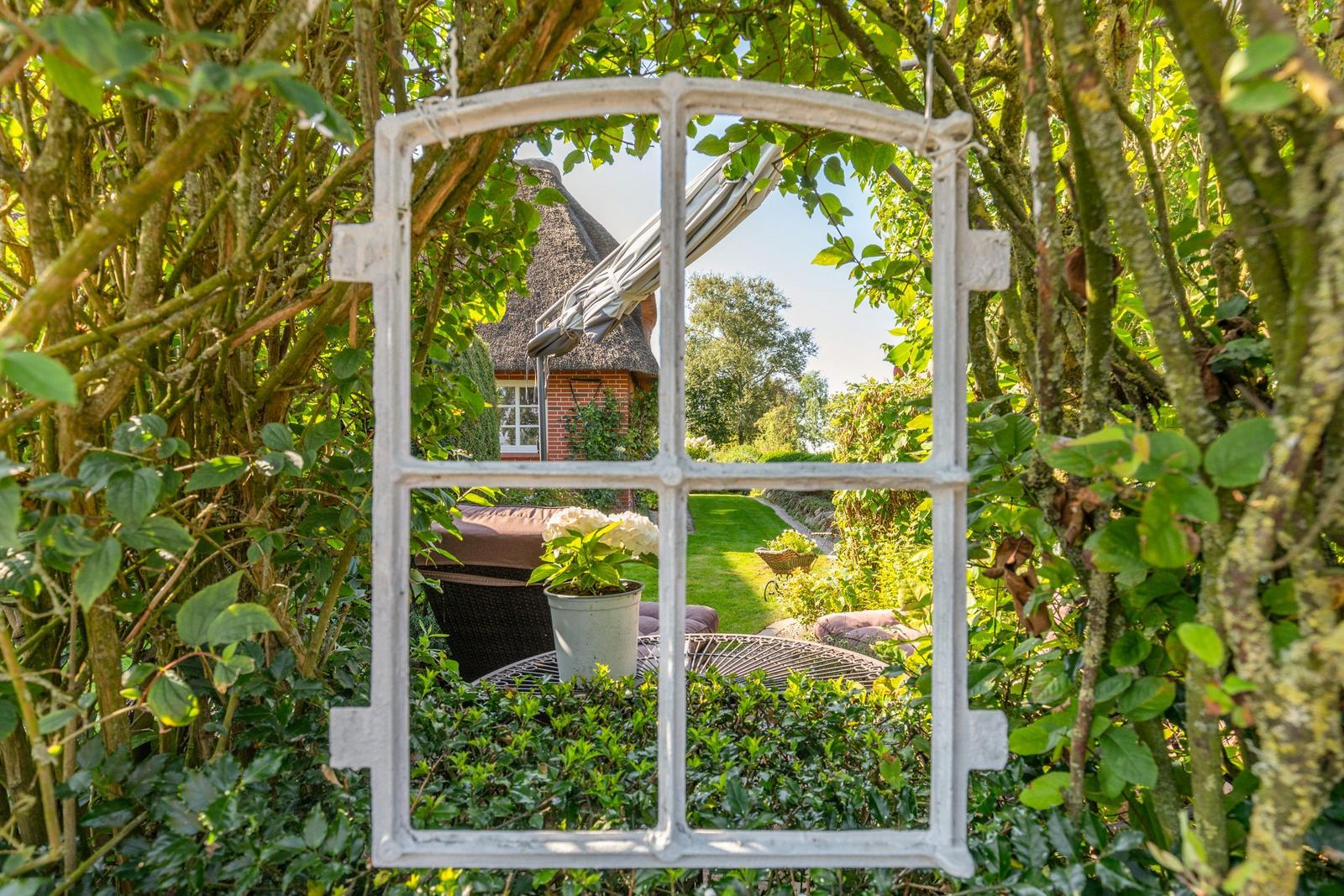 Through a window in the garden, a house with a thatched roof and terrace is visible.